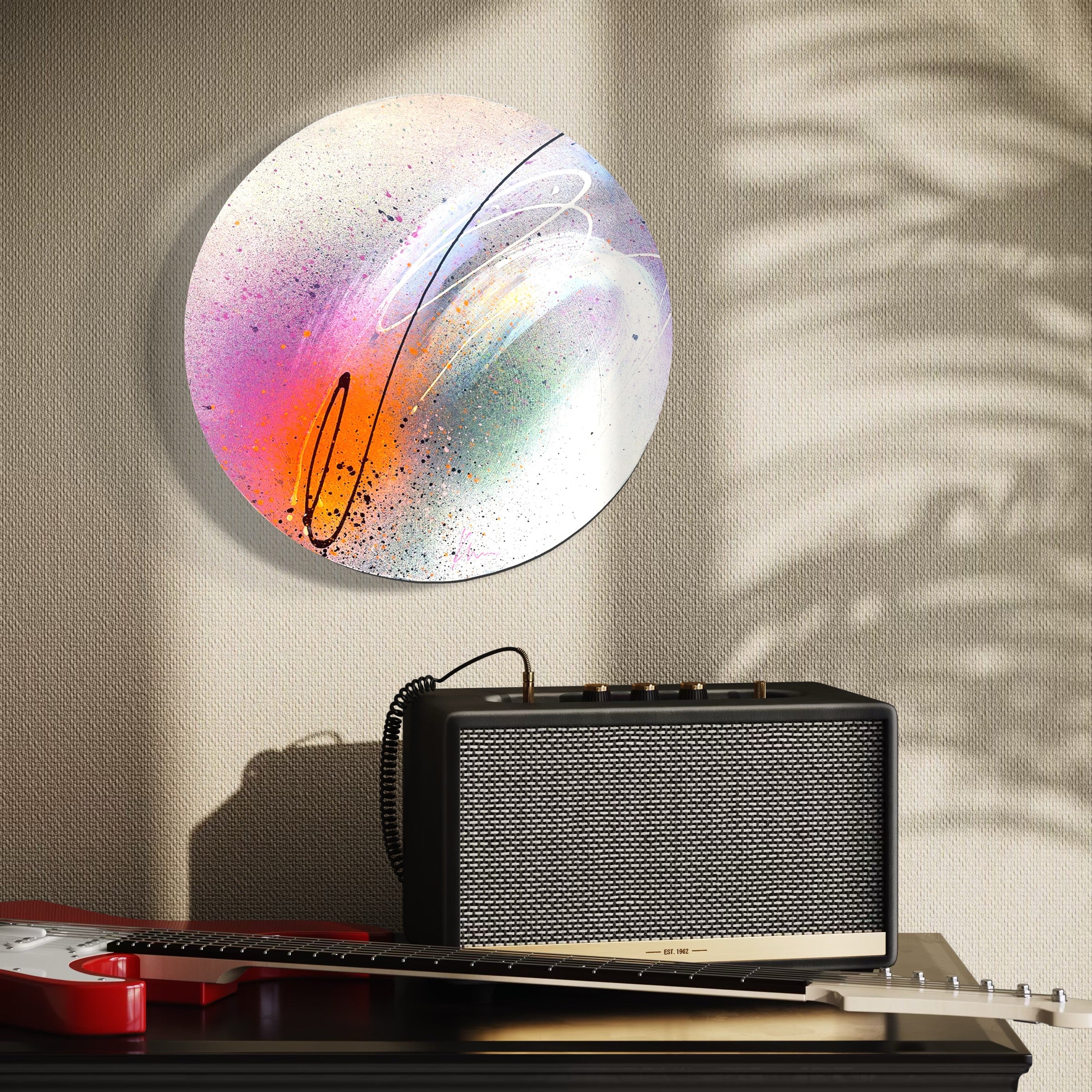 In This Moment" by Kate Mayer on wall, shadow on right; black amplifier and red electric guitar below on table.