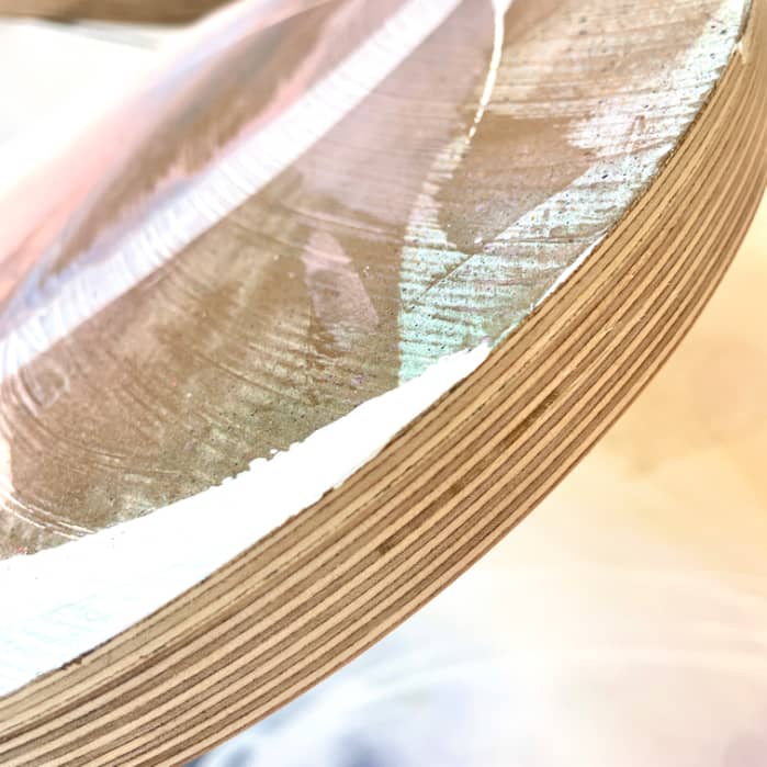 A close-up view of Just Be by Kate Mayer, featuring a stack of plywood with a shiny surface, showcasing the layers and curved edge in soft lighting, perfectly prepped for an abstract painting or a sleek finish with acrylic & spray paint.