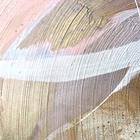 Close-up of the artwork "Just Be" by Kate Mayer, featuring abstract art with sweeping brushstrokes in gold, white, and pink hues. The textured pattern bursts with dynamic energy, enhanced by the creative use of acrylic and spray paint techniques.