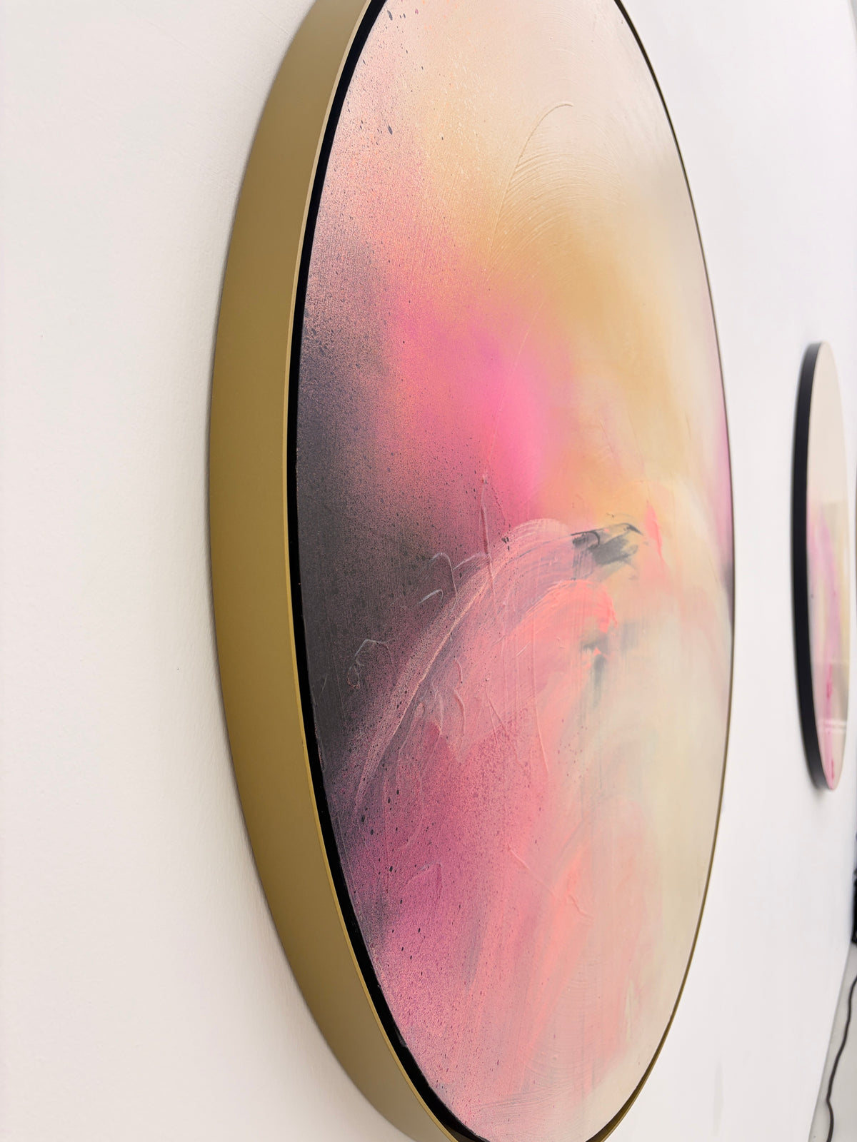 Unfinished Sympathy by Kate Mayer: circular acrylic painting in pink, yellow & black on plywood, framed in metal, side view.