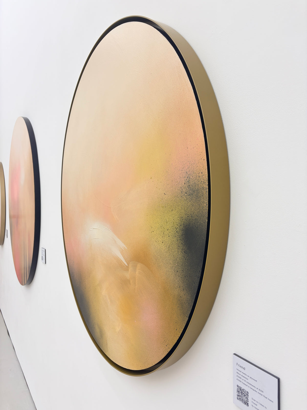 Friend,“ a round abstract canvas by Kate Mayer in soft pastels with handmade metal float frame, hangs on gallery wall.