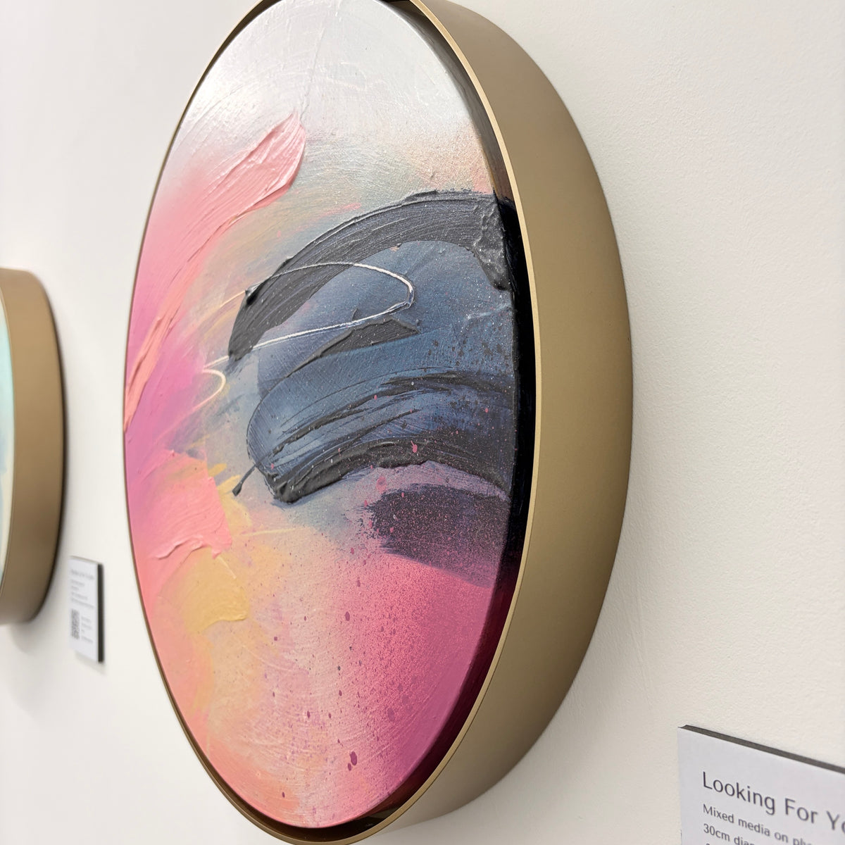 Looking For You“ by Kate Mayer—round abstract acrylic in gold frame, pink/white/blue, on white wall.
