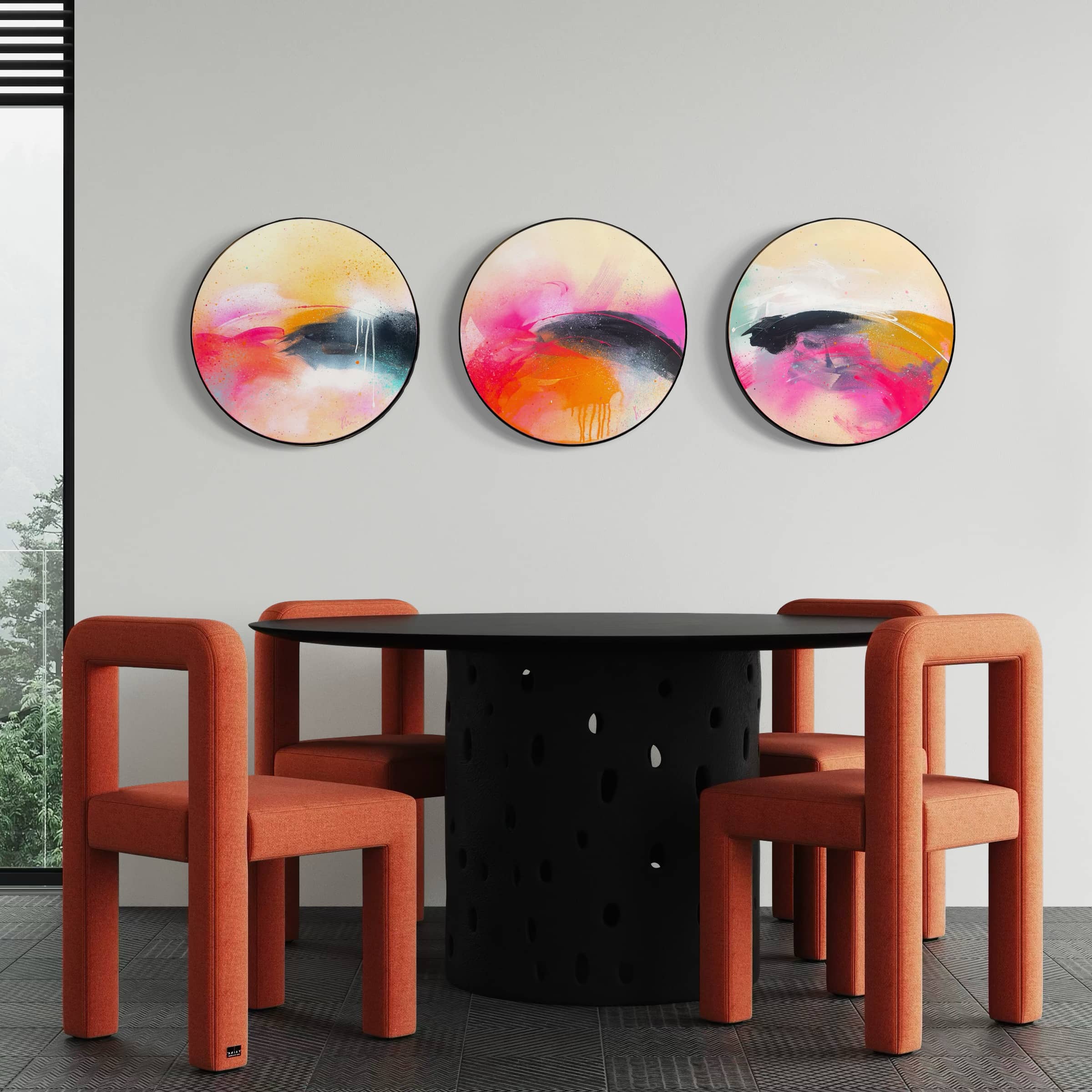 A round black table with four orange chairs and three Kate Mayer Move On Up paintings on a white wall.