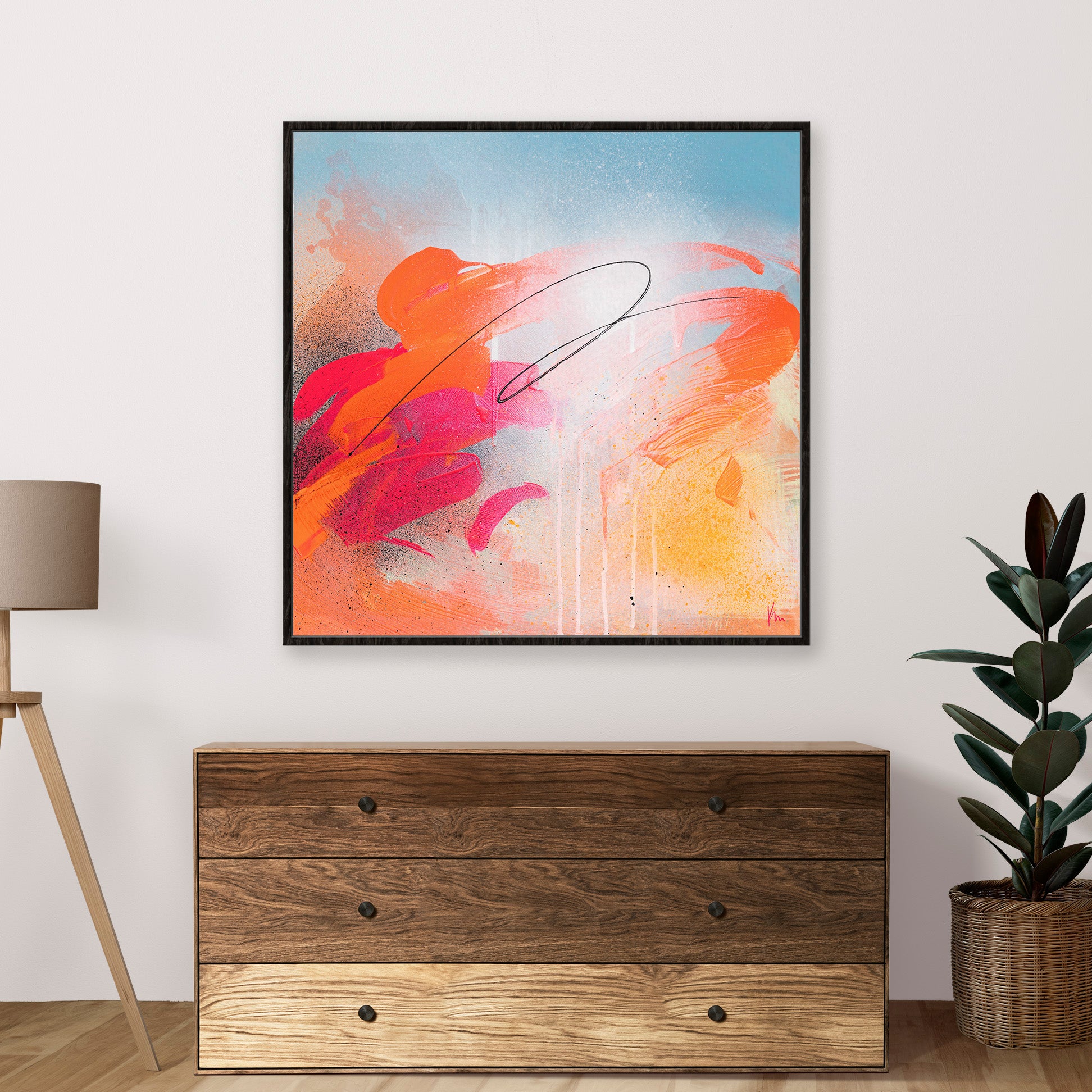 A joyous abstract painting titled *Dance With Me* by Kate Mayer, featuring vibrant colors of orange, pink, and blue hues, adorns the wall above a wooden chest. Beside it, a plant and lamp complete the harmonious setting.