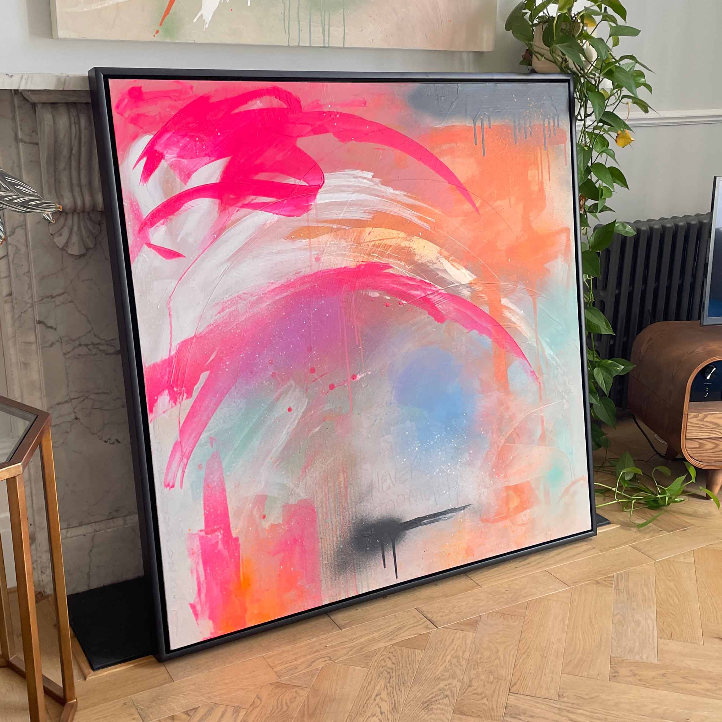 The "Never Too Much - Original Painting" by Kate Mayer showcases vibrant abstract art with bold pink, orange, and black brushstrokes, made with acrylic and spray paint on a canvas resting against a marble fireplace.