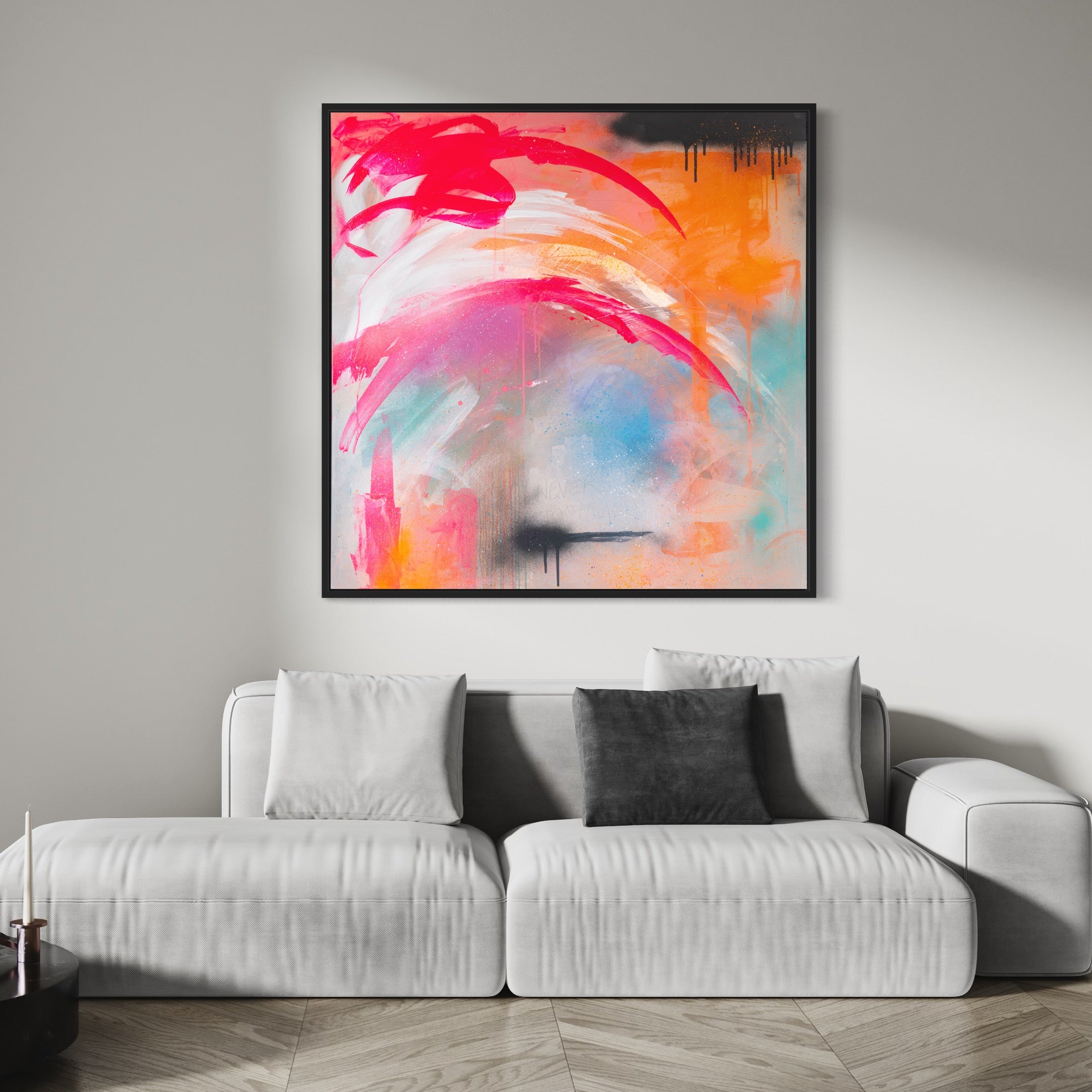 Kate Mayer's original painting, "Never Too Much," crafted with acrylic and spray paint in vibrant pink, orange, and blue tones, is displayed above a modern white sofa featuring a gray pillow in the living room.