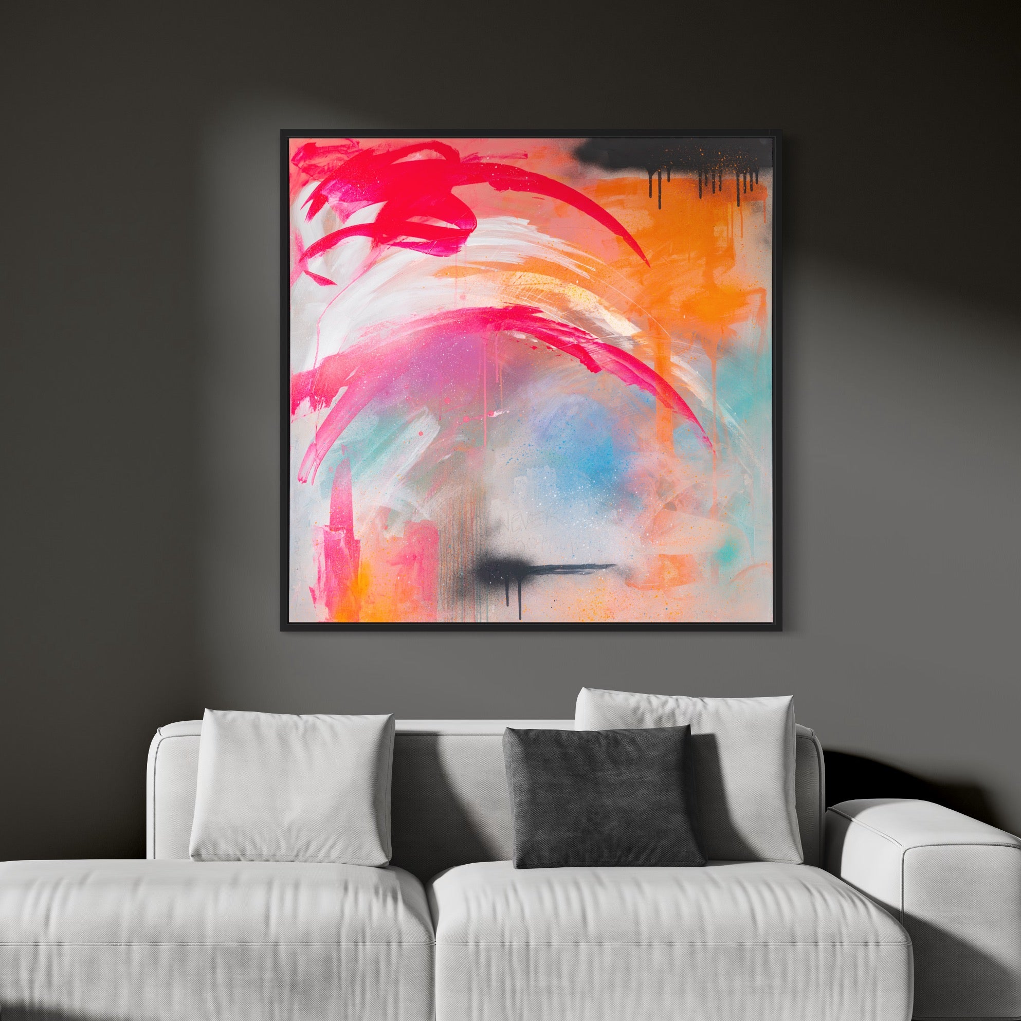 The "Never Too Much" original painting by Kate Mayer beautifully highlights vibrant swirls of red, orange, and blue acrylic and spray paint, displayed on a dark gray wall above a white sofa accented with gray pillows.