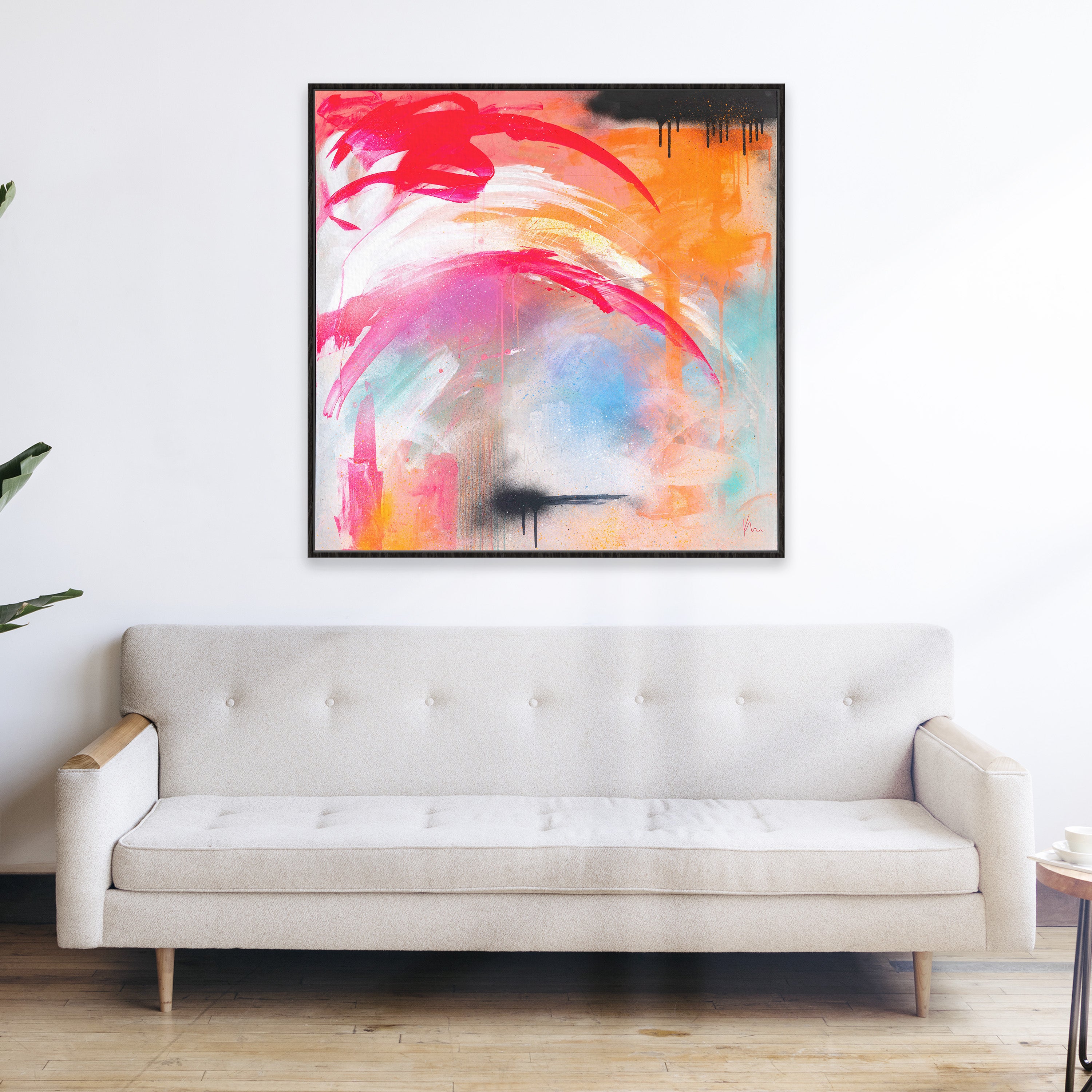 A white sofa is positioned beneath a vibrant abstract painting by Kate Mayer, titled "Never Too Much," featuring bold red, pink, orange, and blue brushstrokes against a pristine white wall.