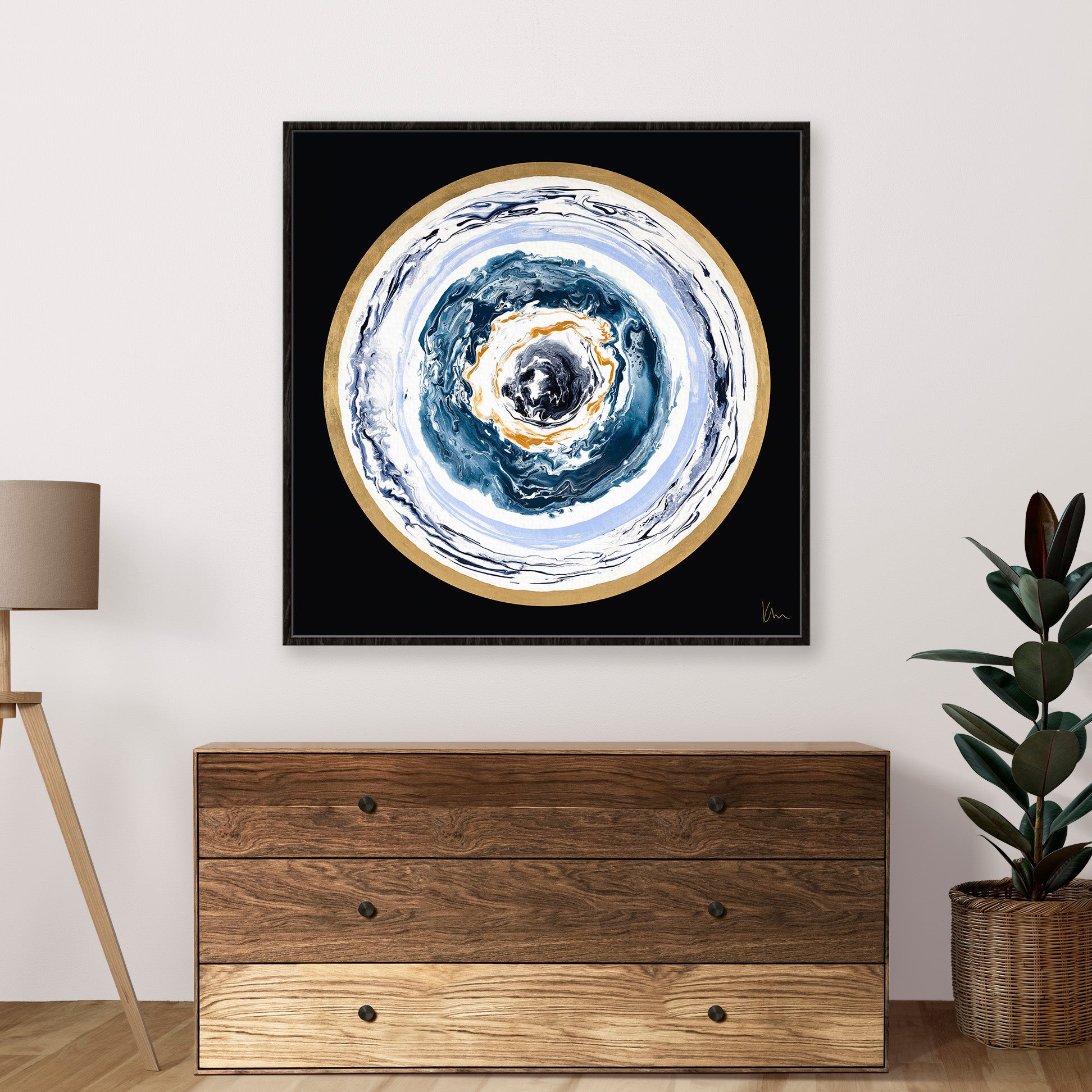 Kate Mayer's "Universal Love" abstract wall art, featuring circular patterns in a square form, hangs above the wooden dresser. A lamp and a potted plant thoughtfully flank the dresser.