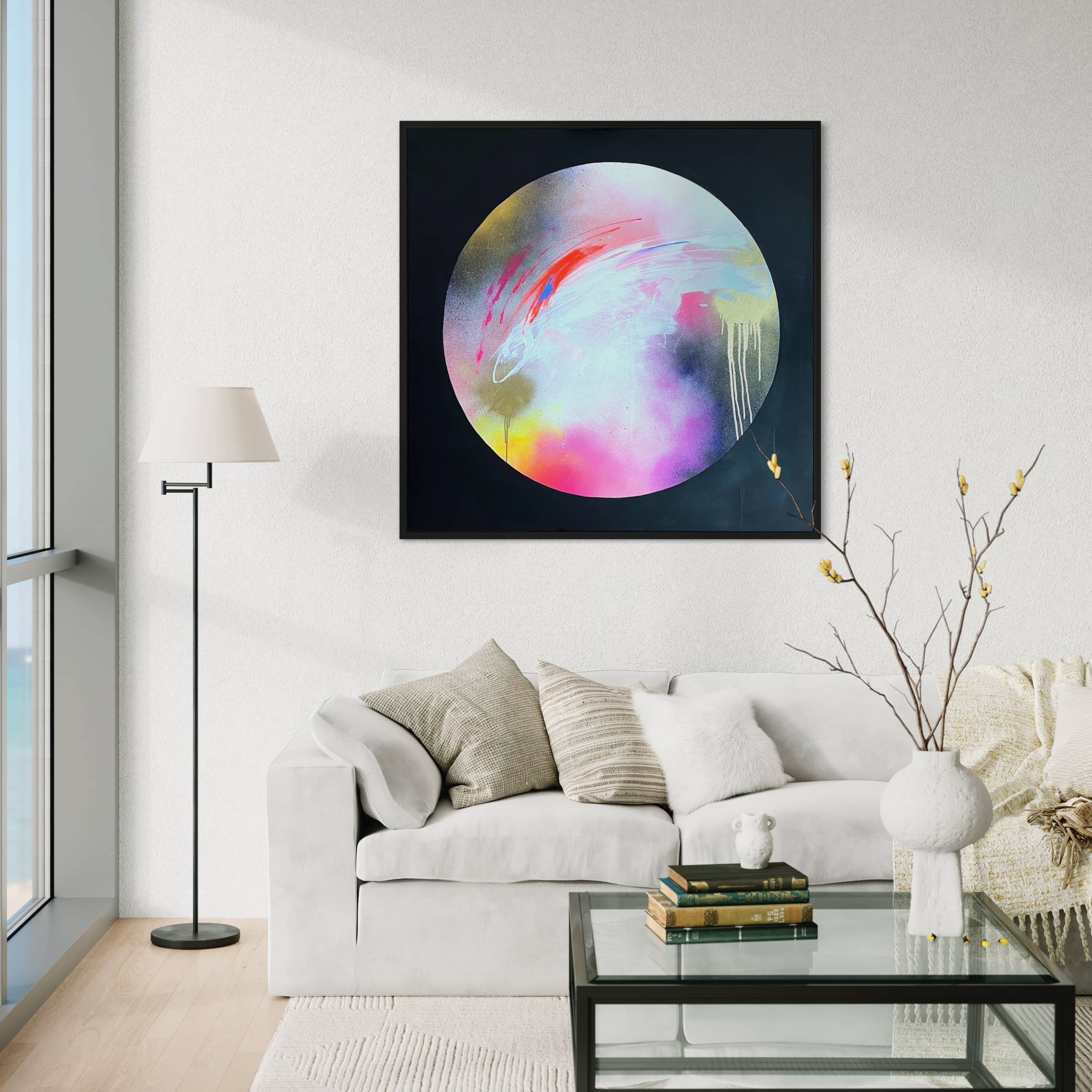 A modern living room with a white sofa, pillows, a glass coffee table, a floor lamp, and "The Dream Starts Here" original painting by Kate Mayer made with acrylic and spray paint on the wall.