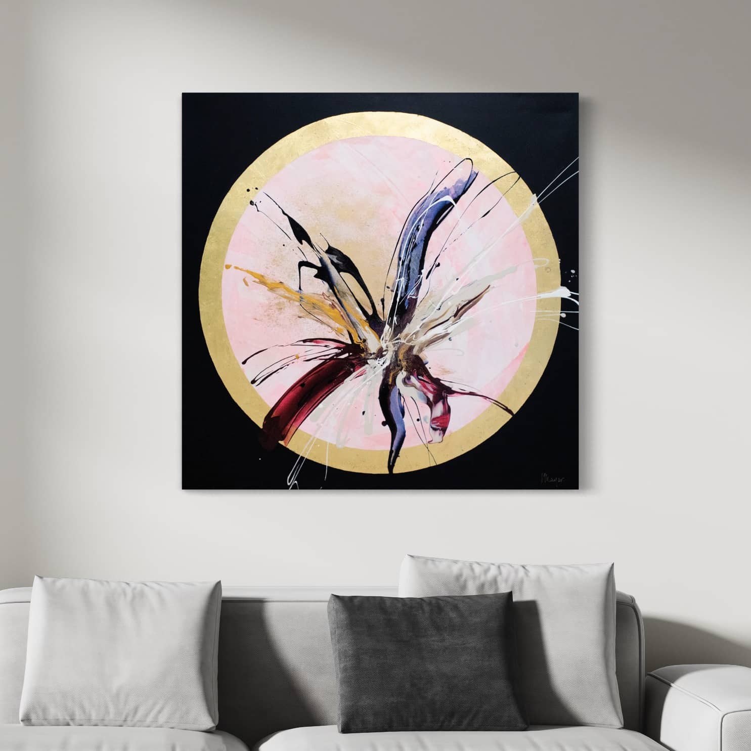 The Innervisions original painting by Kate Mayer, showcasing energetic brushstrokes with acrylic and gold leaf, is displayed in a circular frame above a white couch decorated with three cushions.