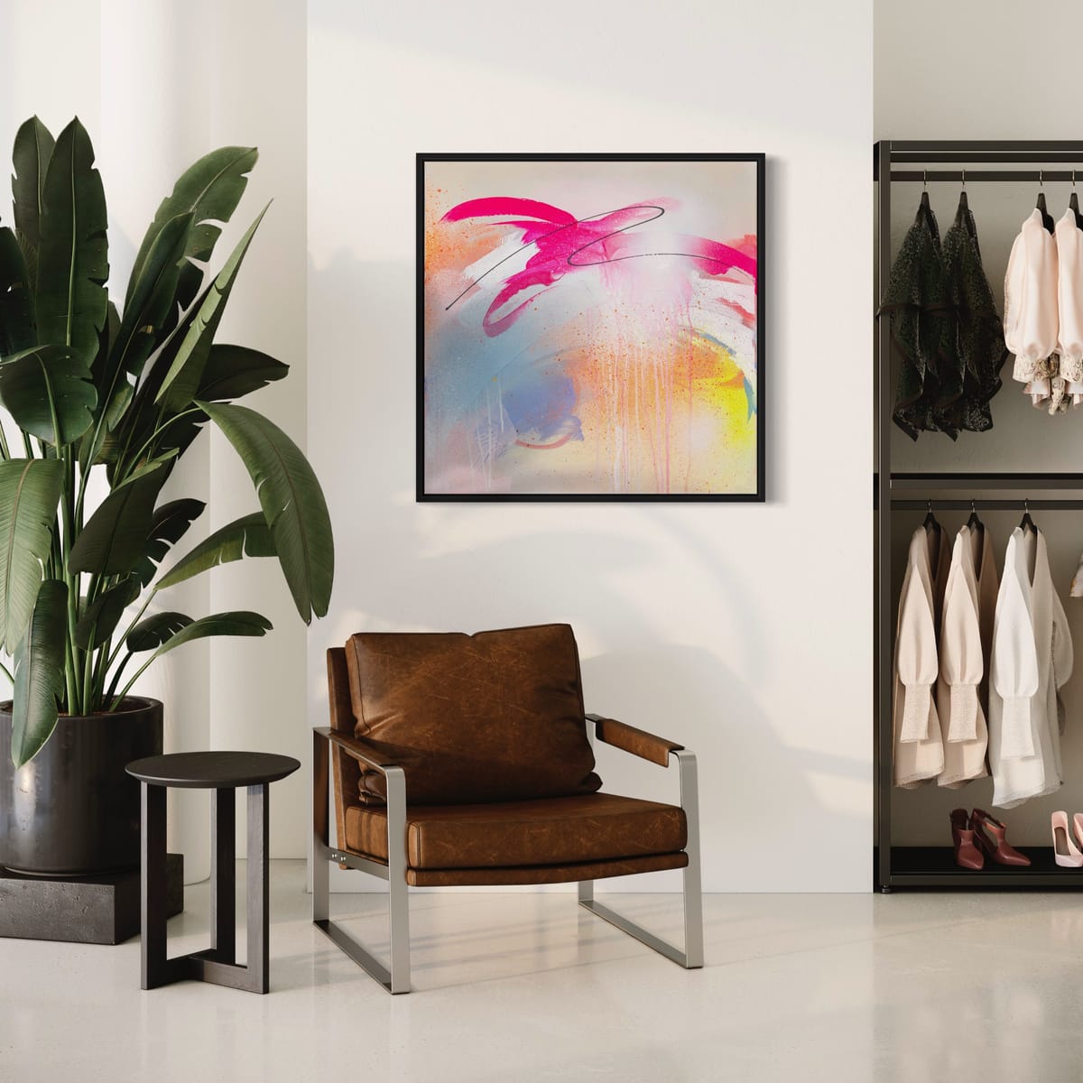The room features a brown chair, side table, and large plant beside an open closet with clothes on hangers. A vibrant painting titled "Hell Yeah" by Kate Mayer graces the wall, adding a splash of creativity to the space.