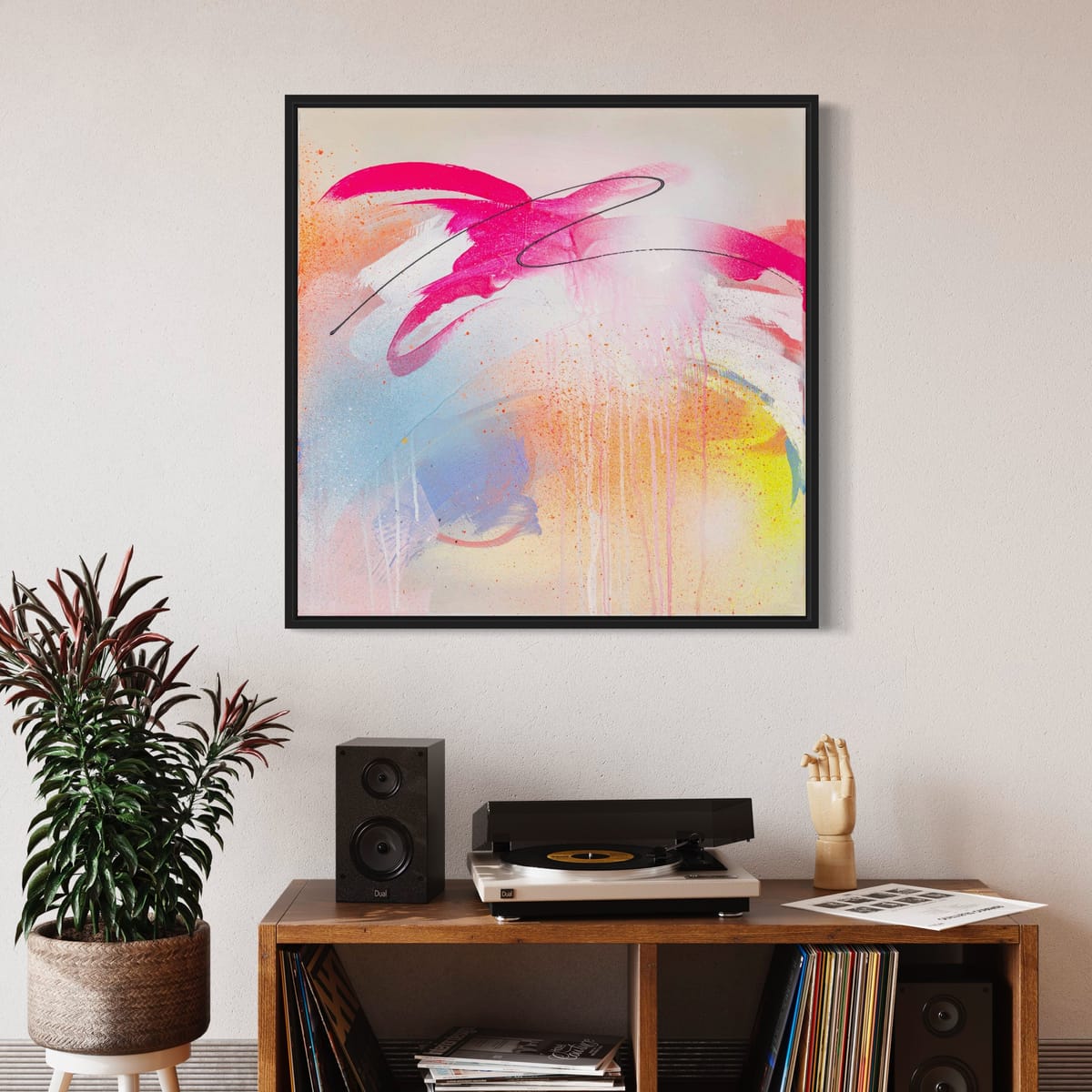 An eclectic setup is created by the vibrant "Hell Yeah - Original Painting" by Kate Mayer, which adorns the wall above a wooden shelf. The shelf features a record player, speakers, a potted plant, and a decorative hand. The artwork's fluorescent paint adds an extra layer of intrigue to this cozy scene.