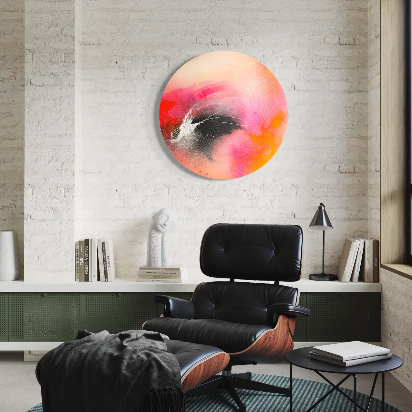 A modern room with an Eames chair, bookshelves, and "Set The World On Fire" by Kate Mayer on a light brick wall.