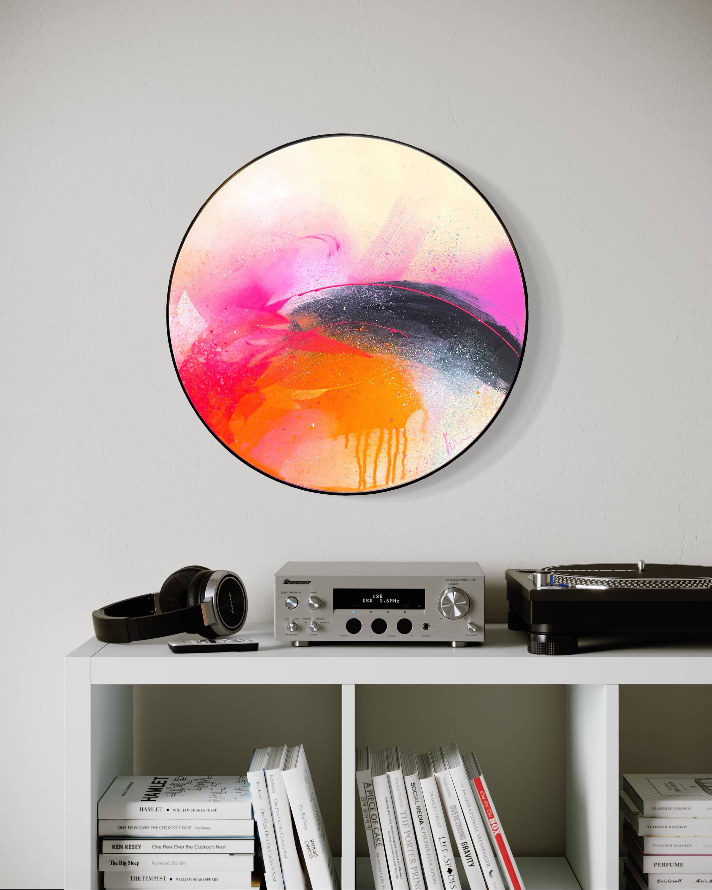 I Carry On" by Kate Mayer: round acrylic art on plywood with pink, orange, and black above a shelf with audio gear and books.