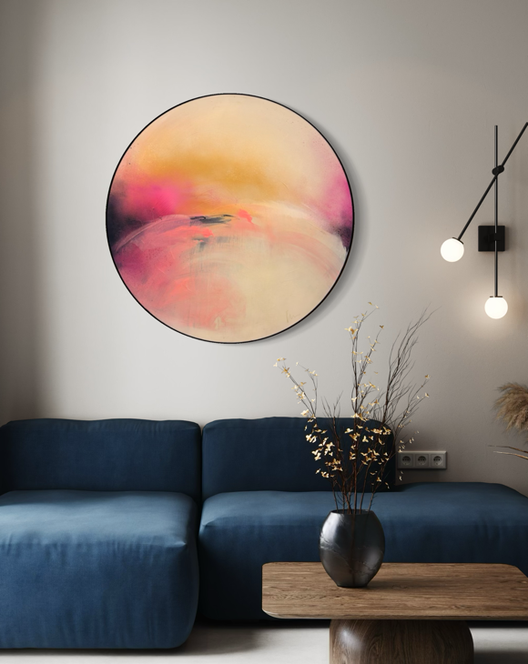 Unfinished Sympathy“ by Kate Mayer, a round abstract in pink/yellow, hangs above a blue sofa in a metal float frame.