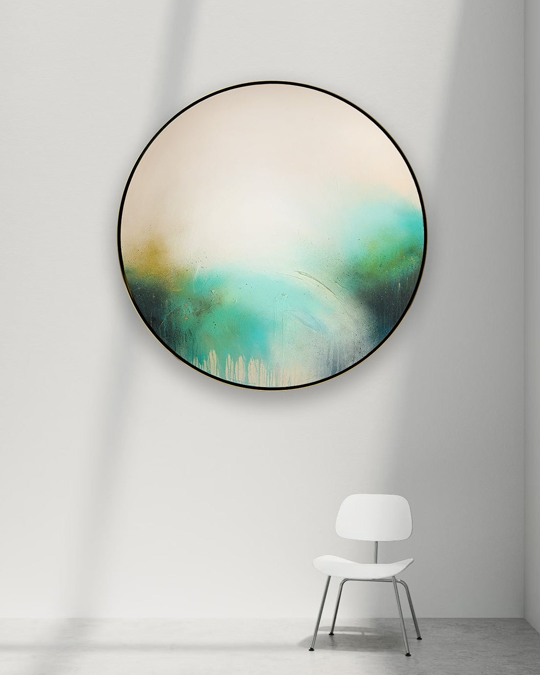 A large round abstract painting by Kate Mayer titled, The Afterglow of Stillness, with teal, green, cream, and gold tones, hanging on a white wall in a minimalist room with a white chair below.