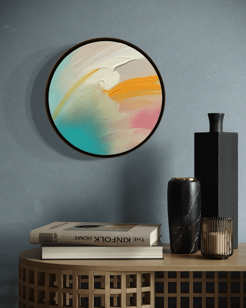 Brighter Day“ by Kate Mayer: round abstract art in a metal float frame above books and vases, blue wall backdrop.
