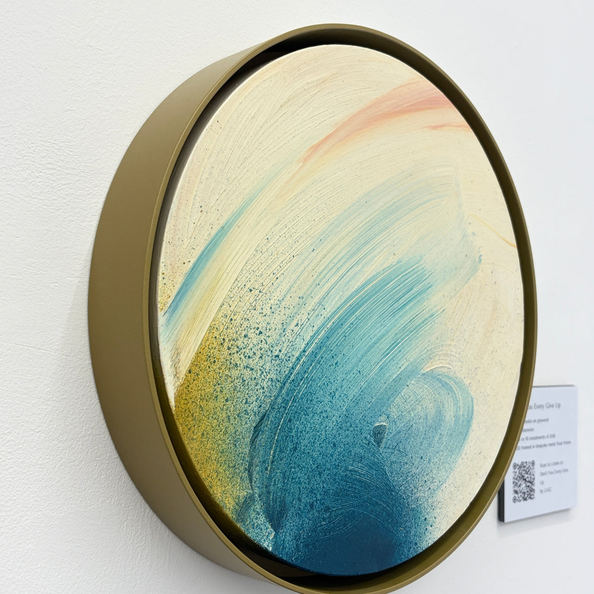 Don’t You Every Give Up“ by Kate Mayer: round abstract painting with blue, yellow & peach strokes, in metal frame.