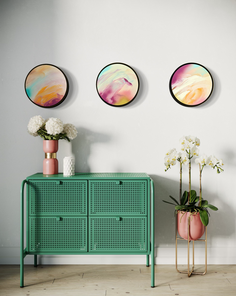 Good Times by Kate Mayer—three acrylic on plywood abstracts above a green cabinet with potted flowers on white wall.
