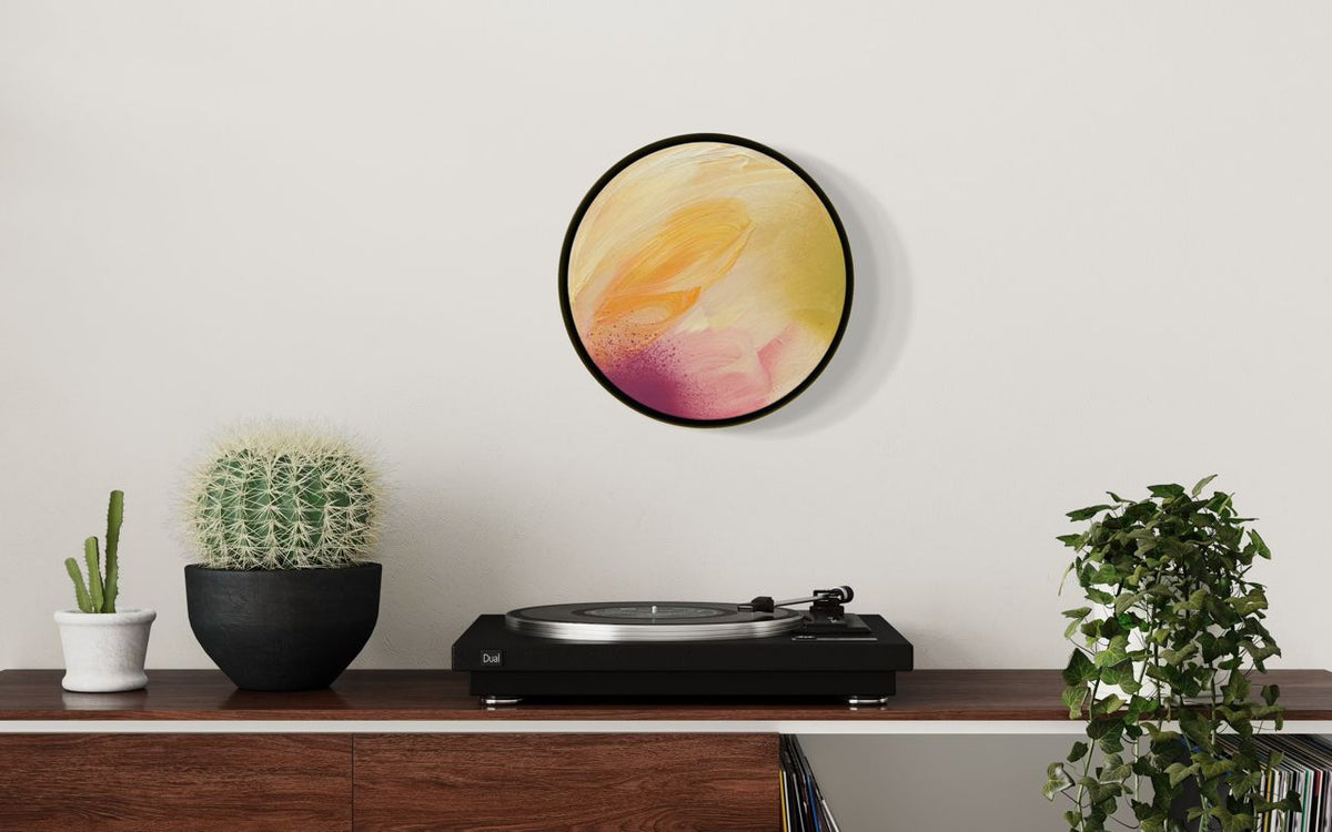 Lovely Day: Abstract artwork by Kate Mayer shown installed in a room. With yellow, orange, and pink tones hanging on a white wall above a wooden console table with a turntable, potted cactus, and green plant.