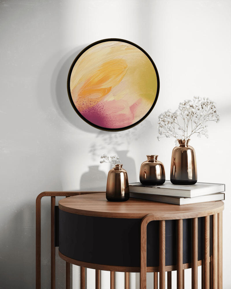 ‘Lovely Day’ by Kate Mayer—a round yellow and pink abstract art above a wooden table with vases, books, and flowers.