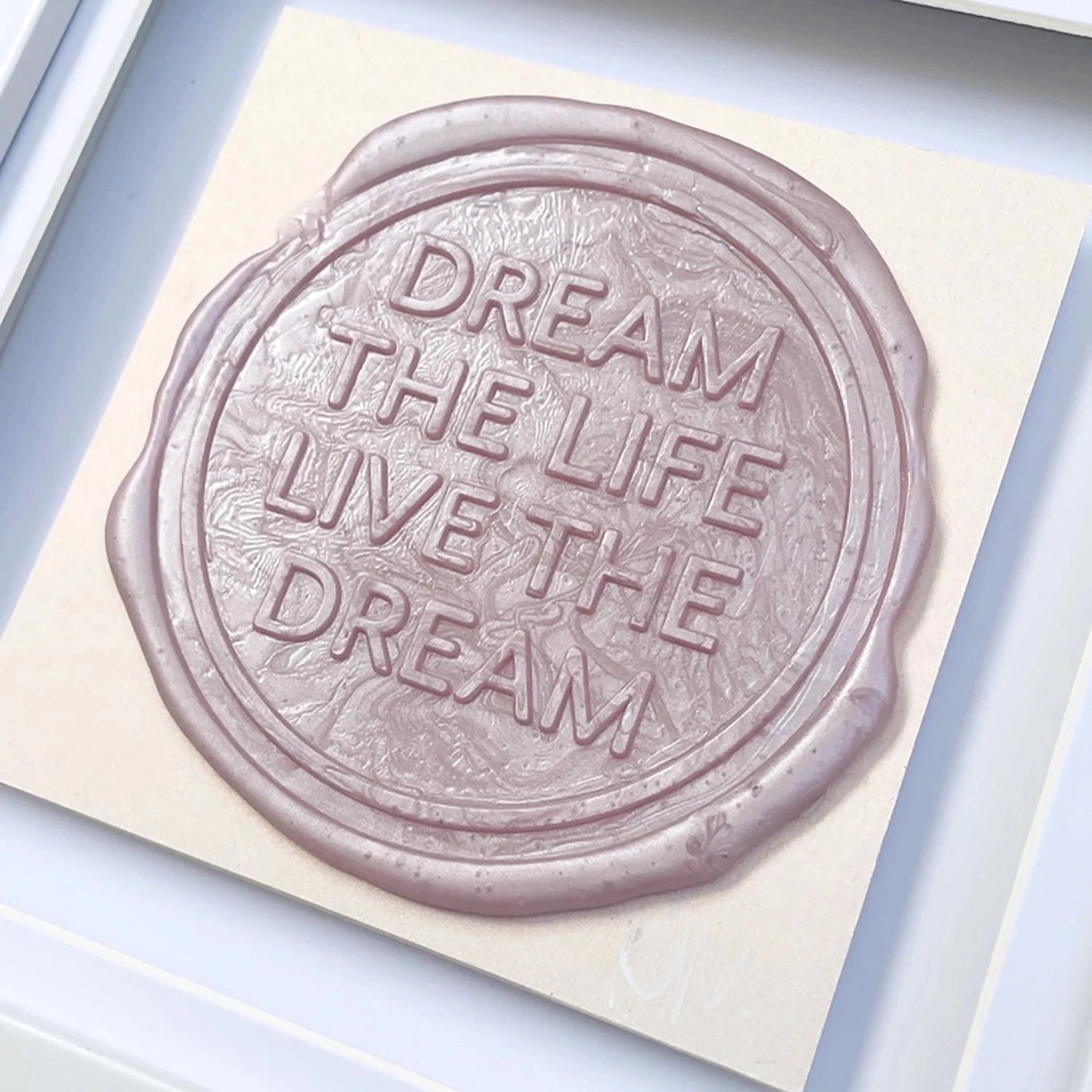 A bespoke wax seal on paper inscribed with "DREAM THE LIFE, LIVE THE DREAM," framed by a white picture frame and signed by the artist, Kate Mayer, from her product line "Sealed Intention to Live The Dream.