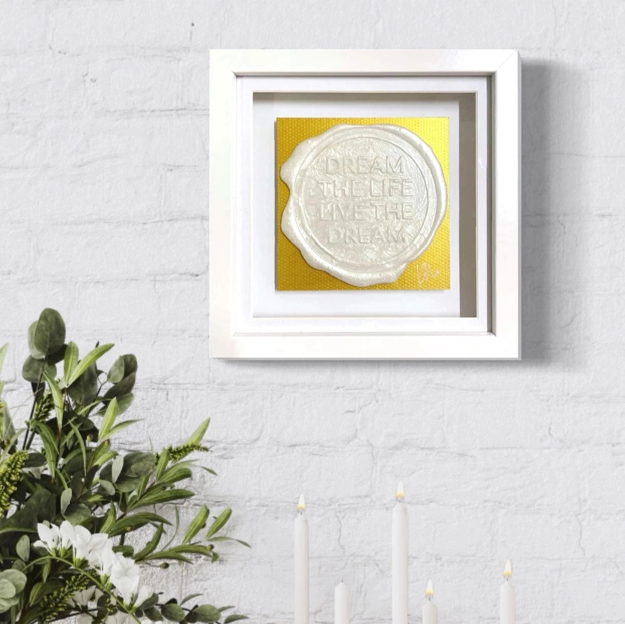 White ceramic vase and candle holders on the table below framed original art titled "Sealed Intention to Live The Dream" by Kate Mayer, featuring the words "Dream the life, live the dream" in white on yellow, signed by the artist.