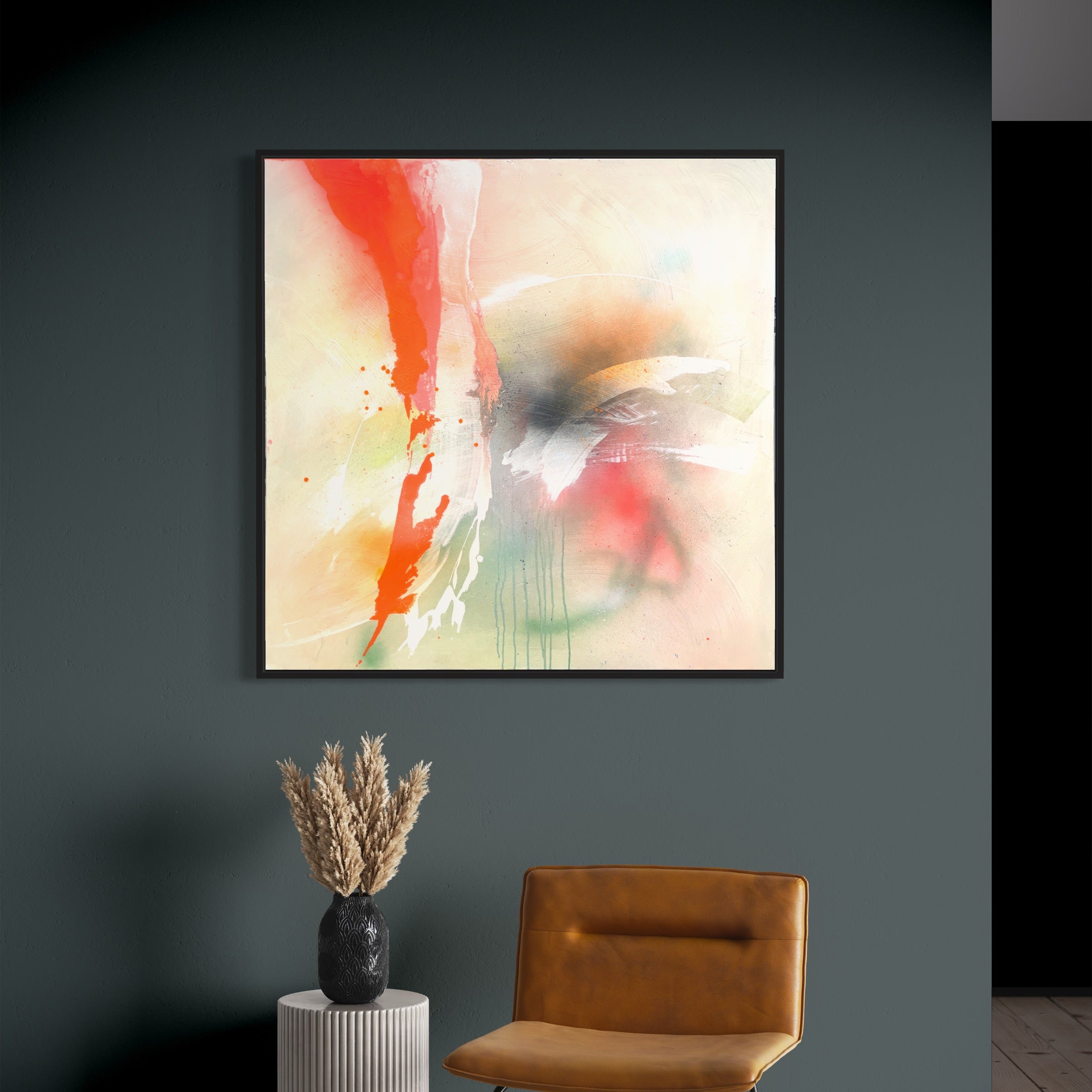 Rainbow Falls," an original painting by Kate Mayer, features bold red, white, and black strokes and is elegantly displayed on a green wall in a sleek black wooden float frame. It rests above a small cylindrical table adorned with dried flowers and is paired with a brown leather chair.