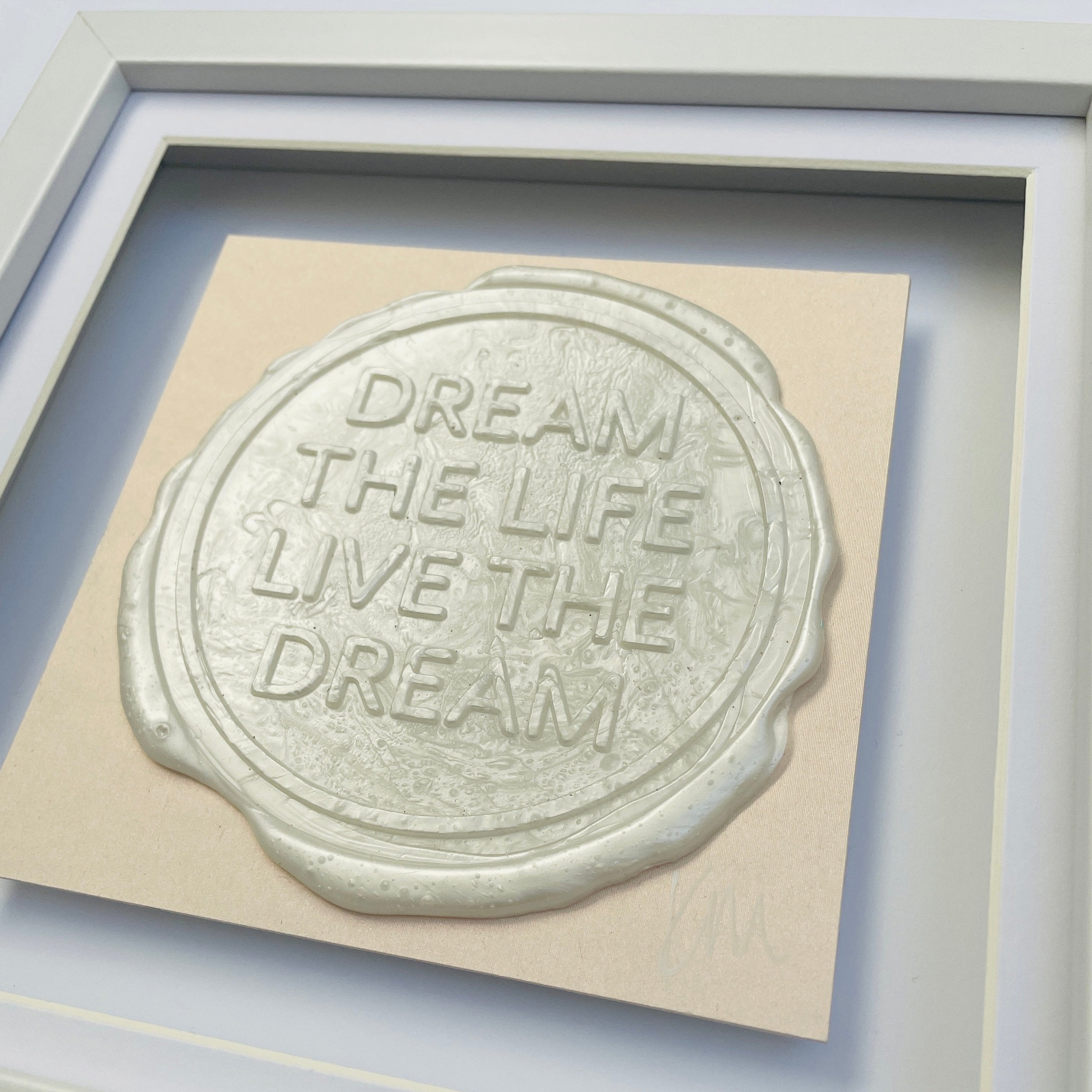 The "Sealed Intention to Live The Dream" by Kate Mayer features a bespoke wax seal with embossed metallic text "DREAM THE LIFE LIVE THE DREAM," beautifully showcased in an original art piece against a light-colored background and elegantly framed within a white shadow frame.