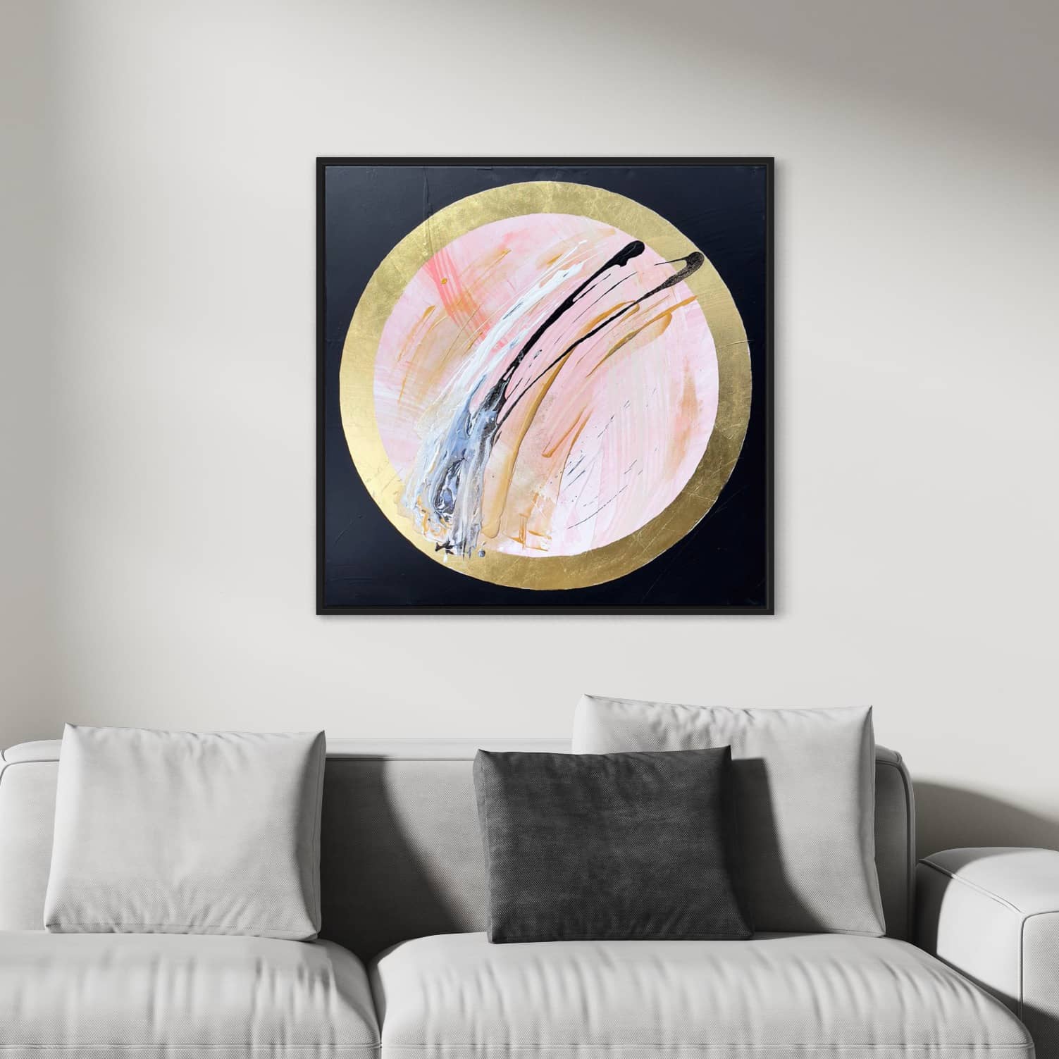 The Let's Go Beyond painting by Kate Mayer, featuring modern abstract artwork with pink, blue, and white acrylic and gold leaf brushstrokes inside a gold circle, is displayed above a light grey sofa.