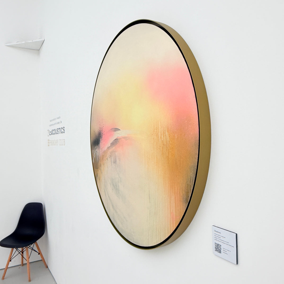 Shadows“ by Kate Mayer: abstract art in pink, yellow & cream, framed in metal float frame beside a black chair.