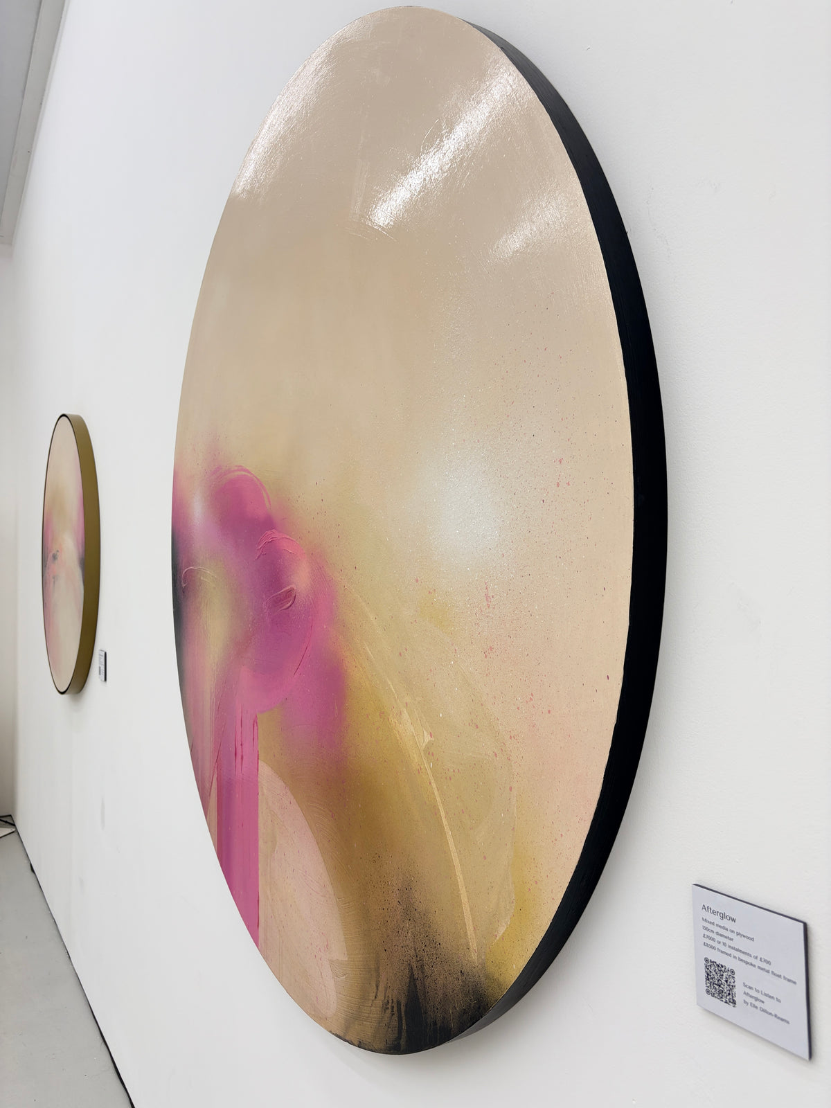 Afterglow“ by Kate Mayer: circular abstract painting in pink, gold & black with diamond dust on white gallery wall.