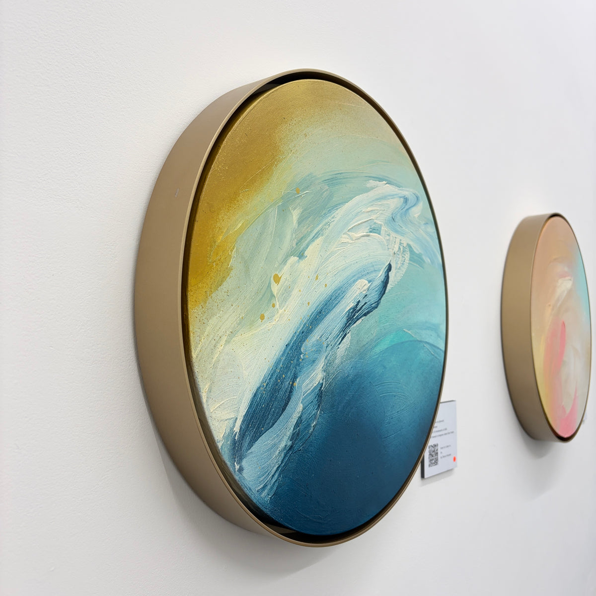 As“ by Kate Mayer: Round abstract painting in blue, white & gold acrylic on plywood with a handmade metal frame.