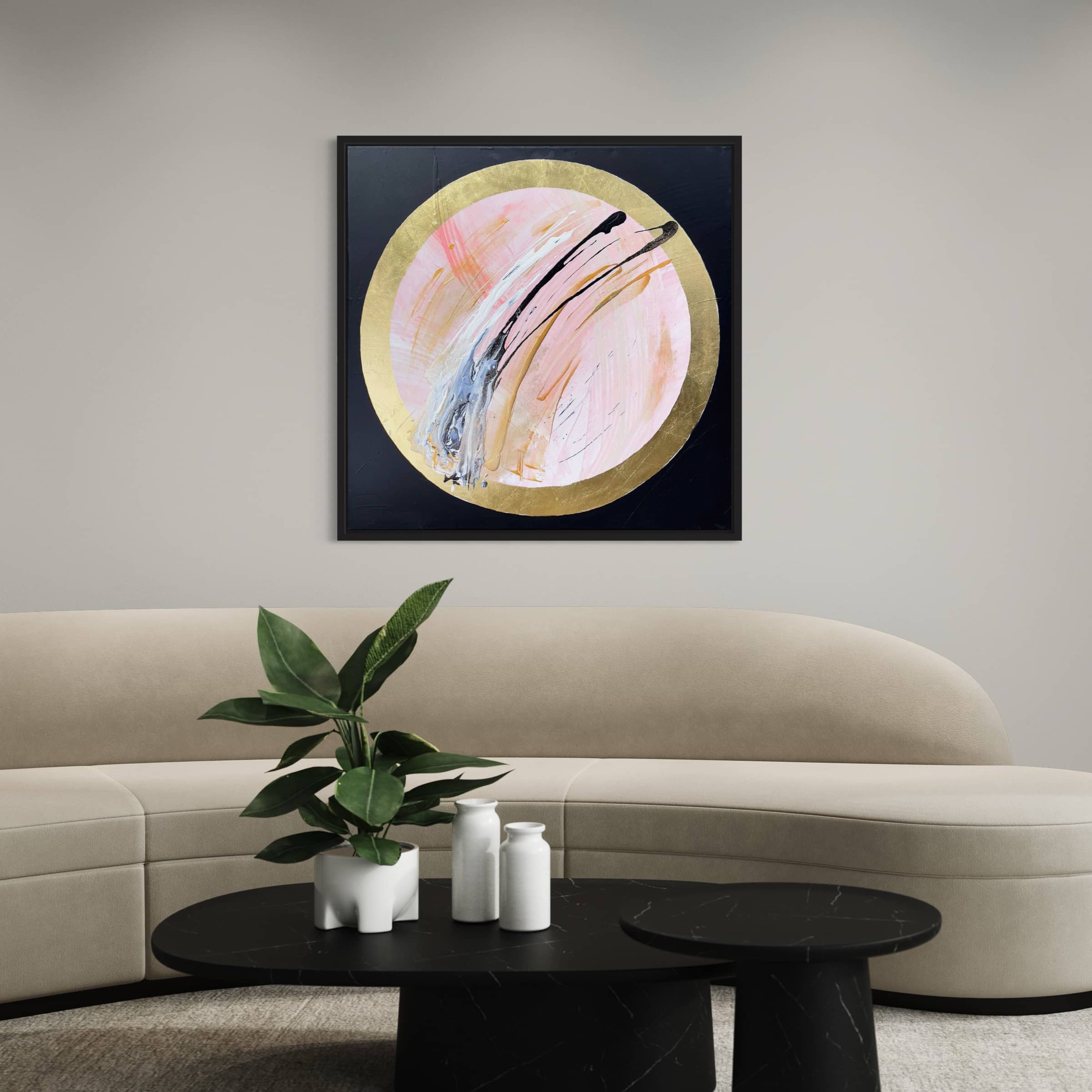 A beige curved sofa with a potted plant and decor on black coffee tables, featuring "Let's Go Beyond," an original abstract painting by Kate Mayer in acrylic and gold leaf, framed on a light gray wall.