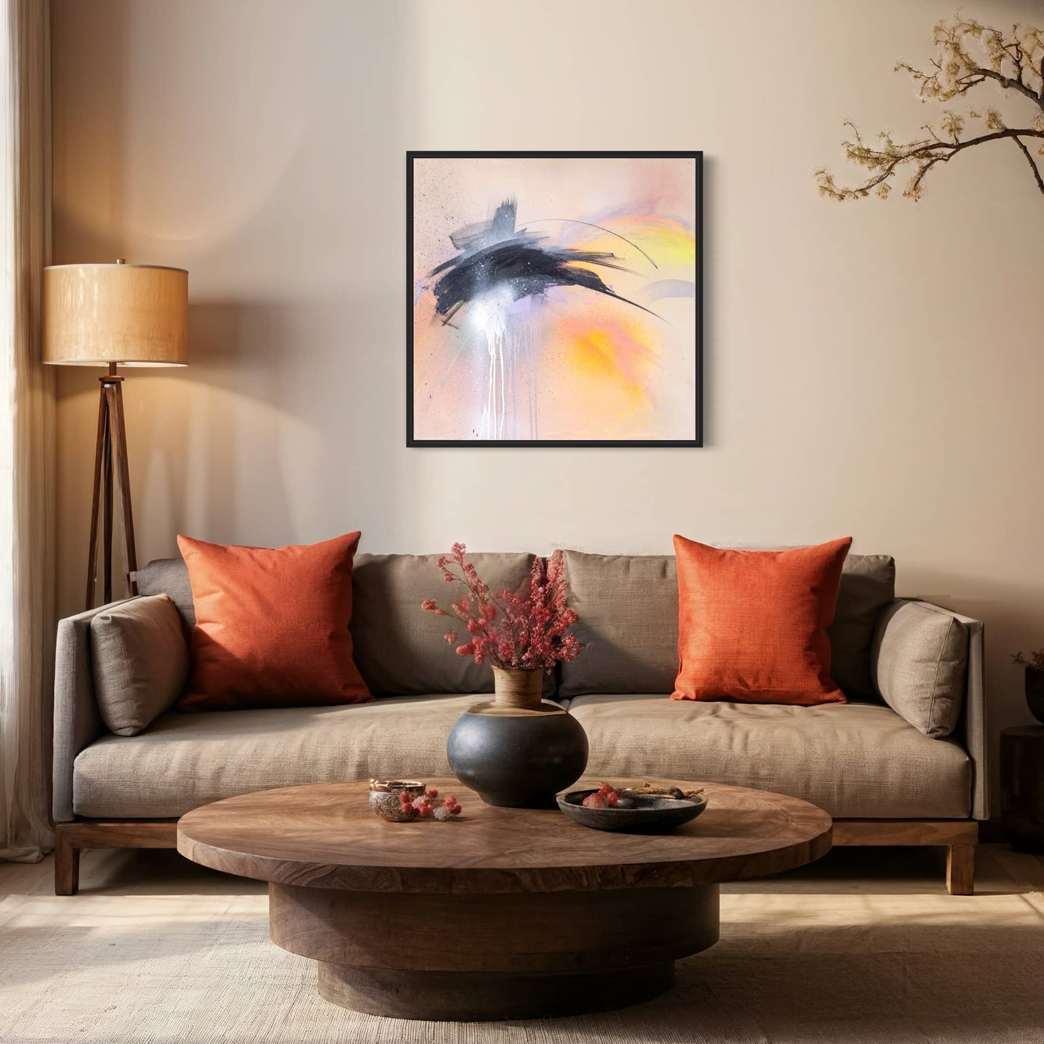 A cozy living room featuring a gray sofa adorned with orange pillows, a round wooden coffee table, a floor lamp, decorative branches, and "That Moment On Black Sand Beach" - an original painting by Kate Mayer created with acrylic and spray paint. The abstract artwork is accompanied by a certificate of authentication.