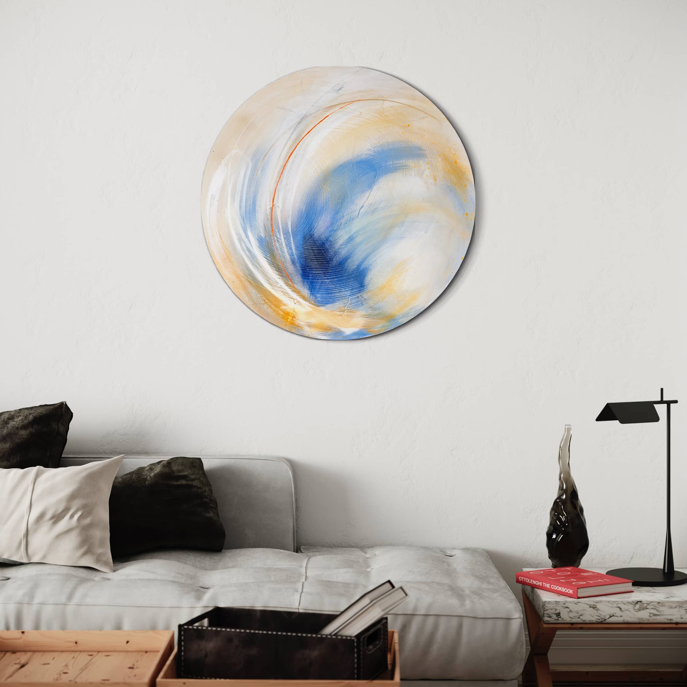 The Go Your Own Way original painting by Kate Mayer, showcasing blue, yellow, and white swirls crafted with acrylic and spray paint, adorns a white wall above a modern sofa. The artwork is perfectly complemented by pillows and a sleek side table.