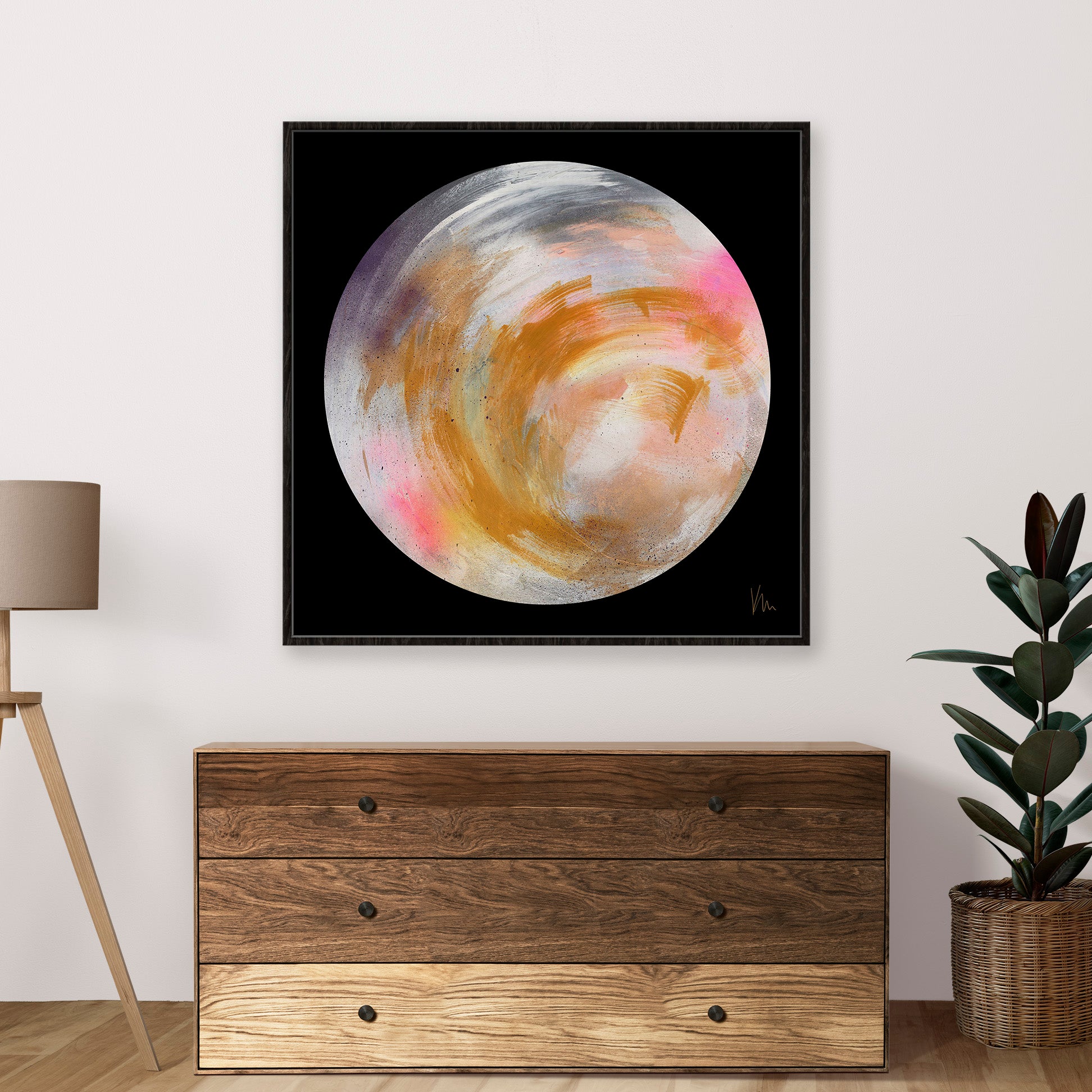 The "Dream Believer" abstract painting from Kate Mayer, depicting a colorful planet against a black backdrop to spark the imagination, is elegantly showcased above a wooden dresser, accompanied by a plant and lamp.