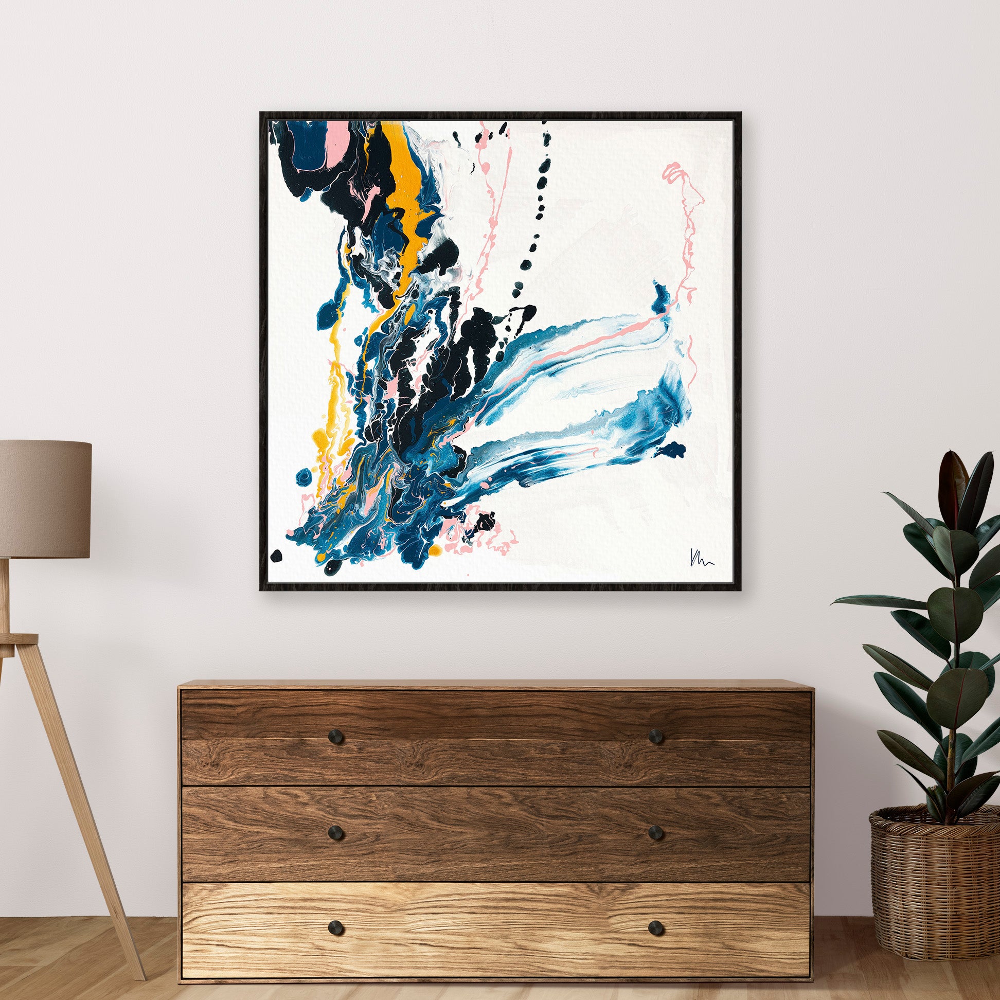 The "Emerging" abstract painting by Kate Mayer, featuring swirling blue, yellow, and pink colors that symbolize new beginnings, is displayed above a wooden dresser next to a lamp and plant.