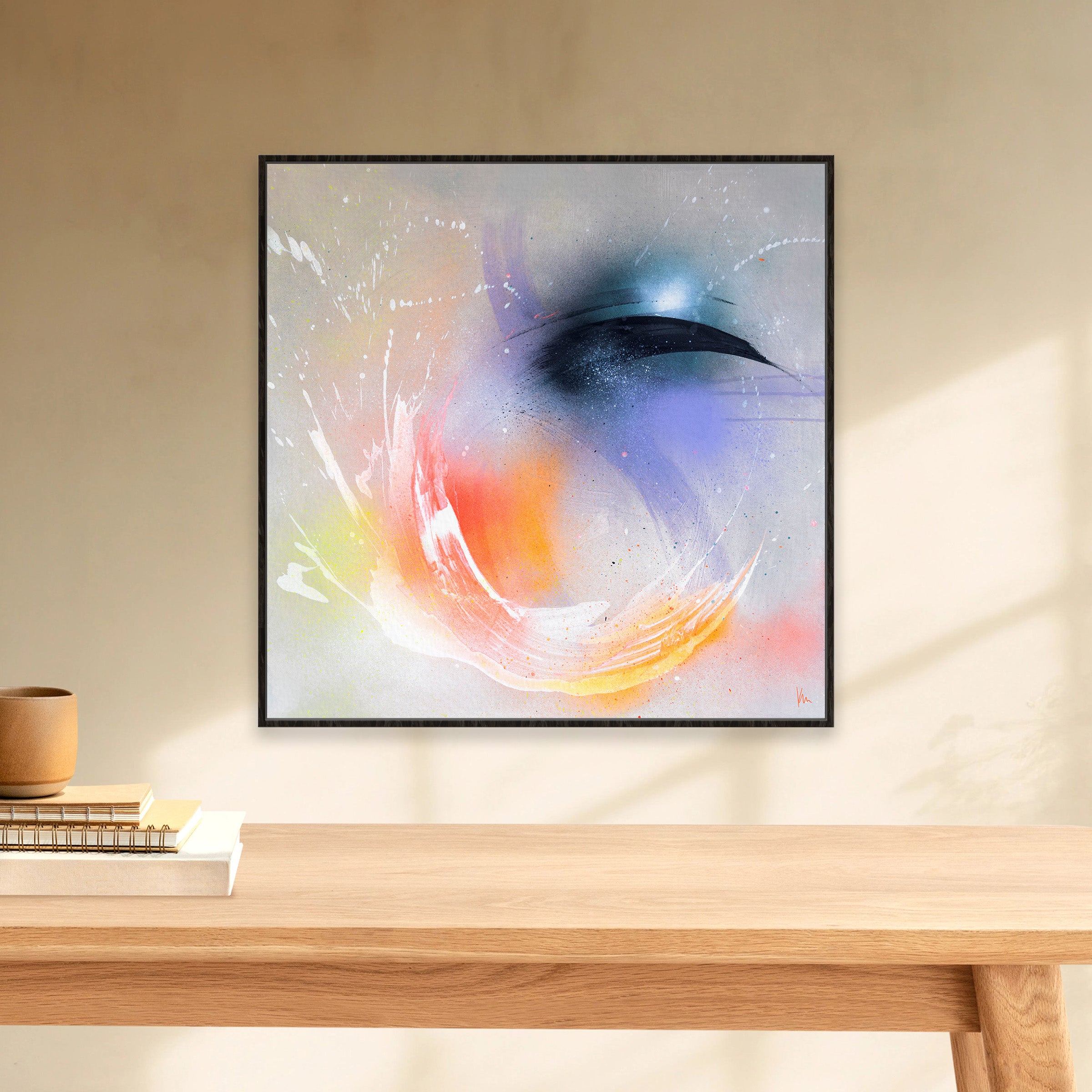 The art piece "Eternal Vitality" by Kate Mayer features swirling colors of white, orange, and blue, offering a magical backdrop. Elegantly framed, it adorns a beige wall above a wooden table, evoking the ethereal landscapes of Iceland.