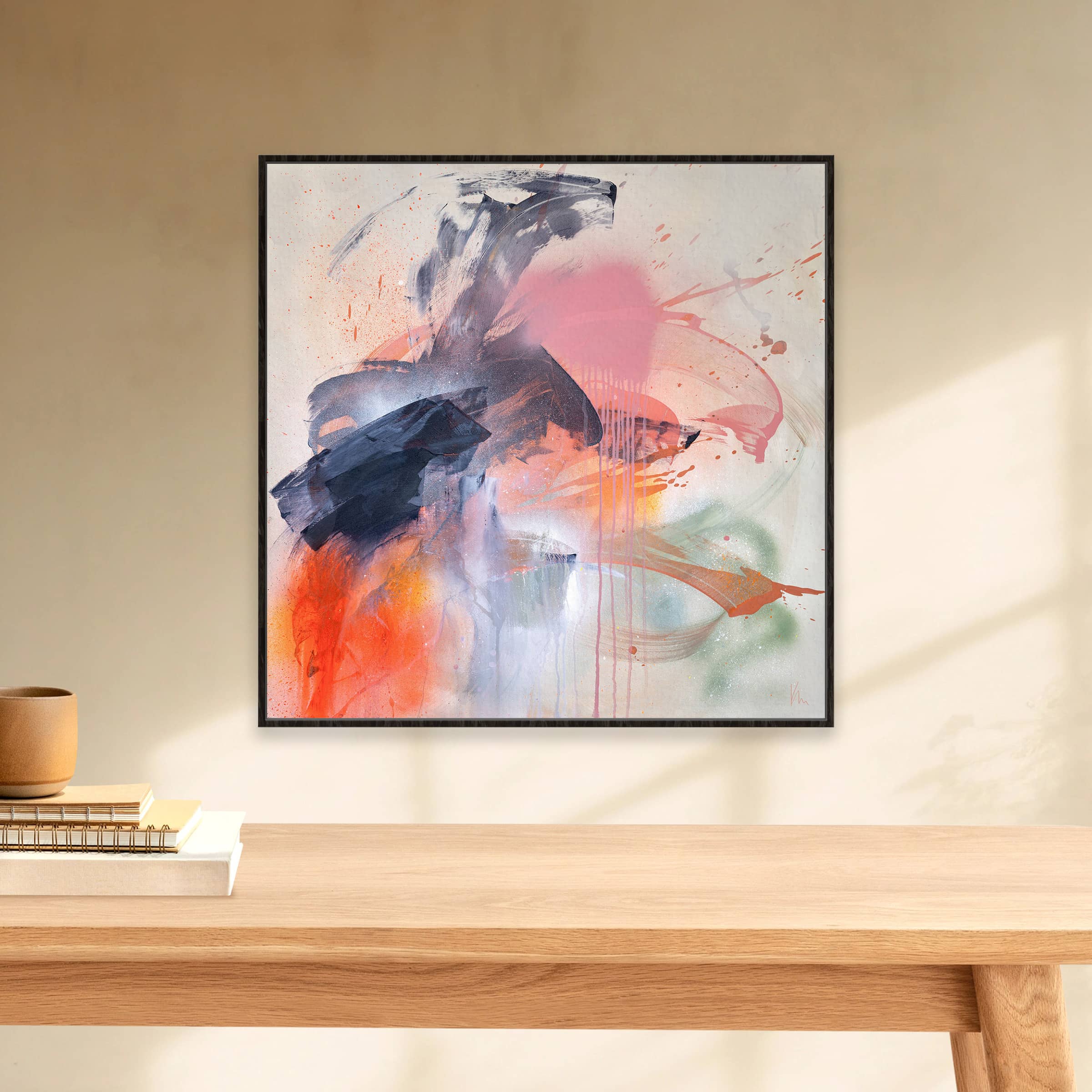 Kate Mayer's 'Fire And Ice' is an abstract masterpiece featuring bold strokes of pink, blue, orange, and gray, beautifully displayed on a light-colored wall above a minimalist wooden table.