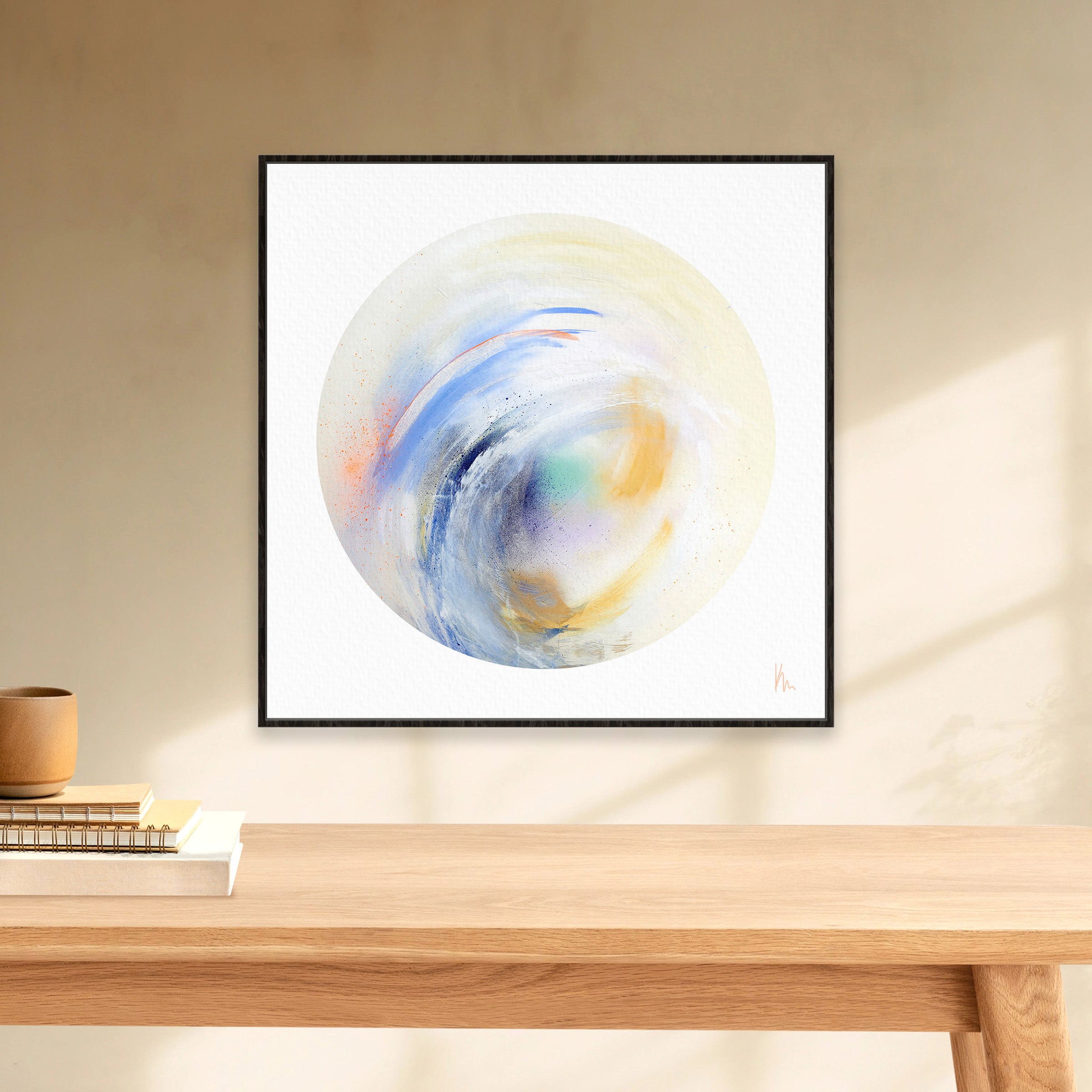 The "Free Spirit" painting by Kate Mayer captures the coastal beauty in a swirling circle with blue, orange, and green tones. It hangs elegantly in a minimalist room above a light wooden table, inviting you to embrace the free spirit within.