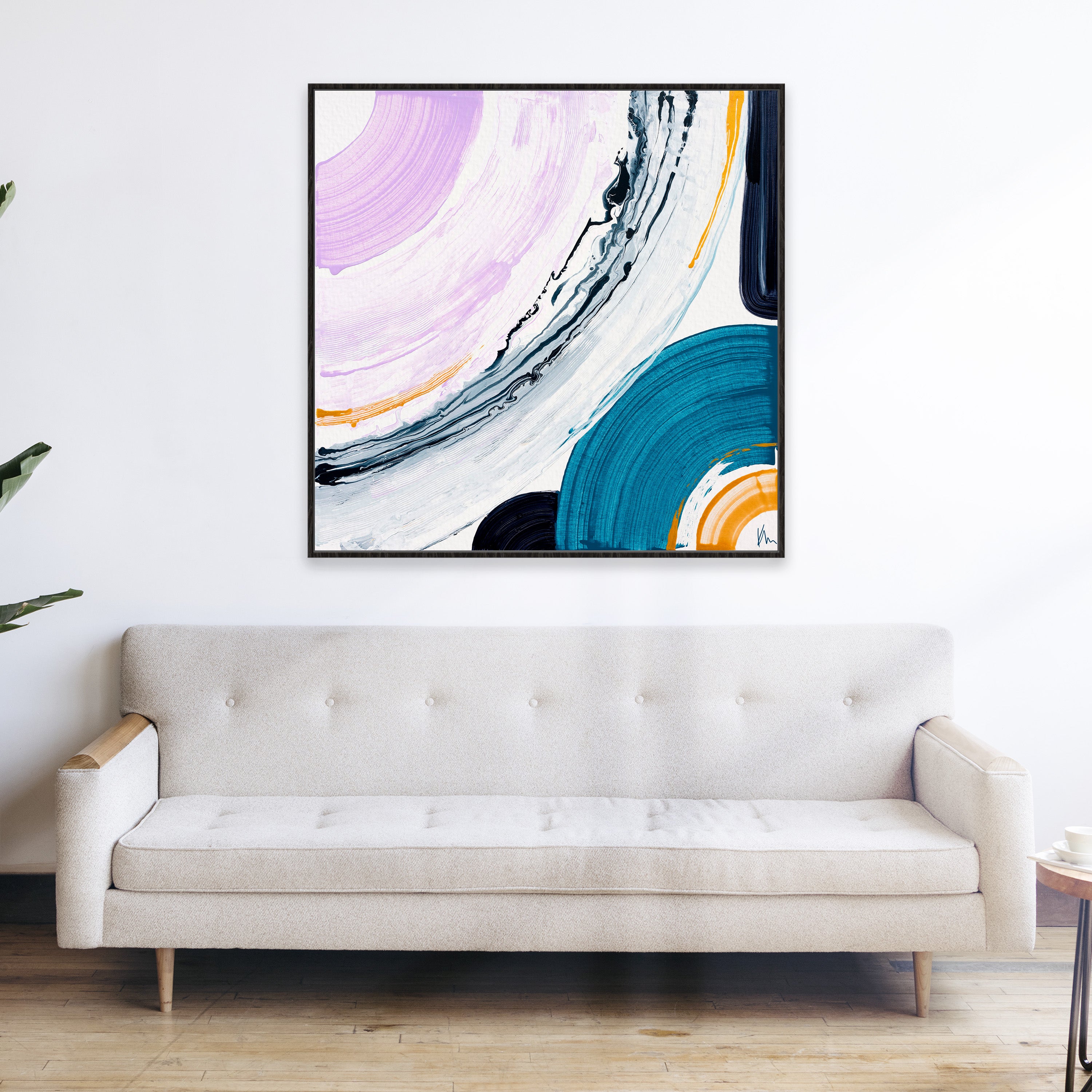 A minimalist room with a cream sofa is beautifully accented by Kate Mayer's "Me & You" abstract painting on the wall, featuring swirls of pink, black, and teal. Adding vibrancy to the serene space, this artistic touch embodies modern elegance.