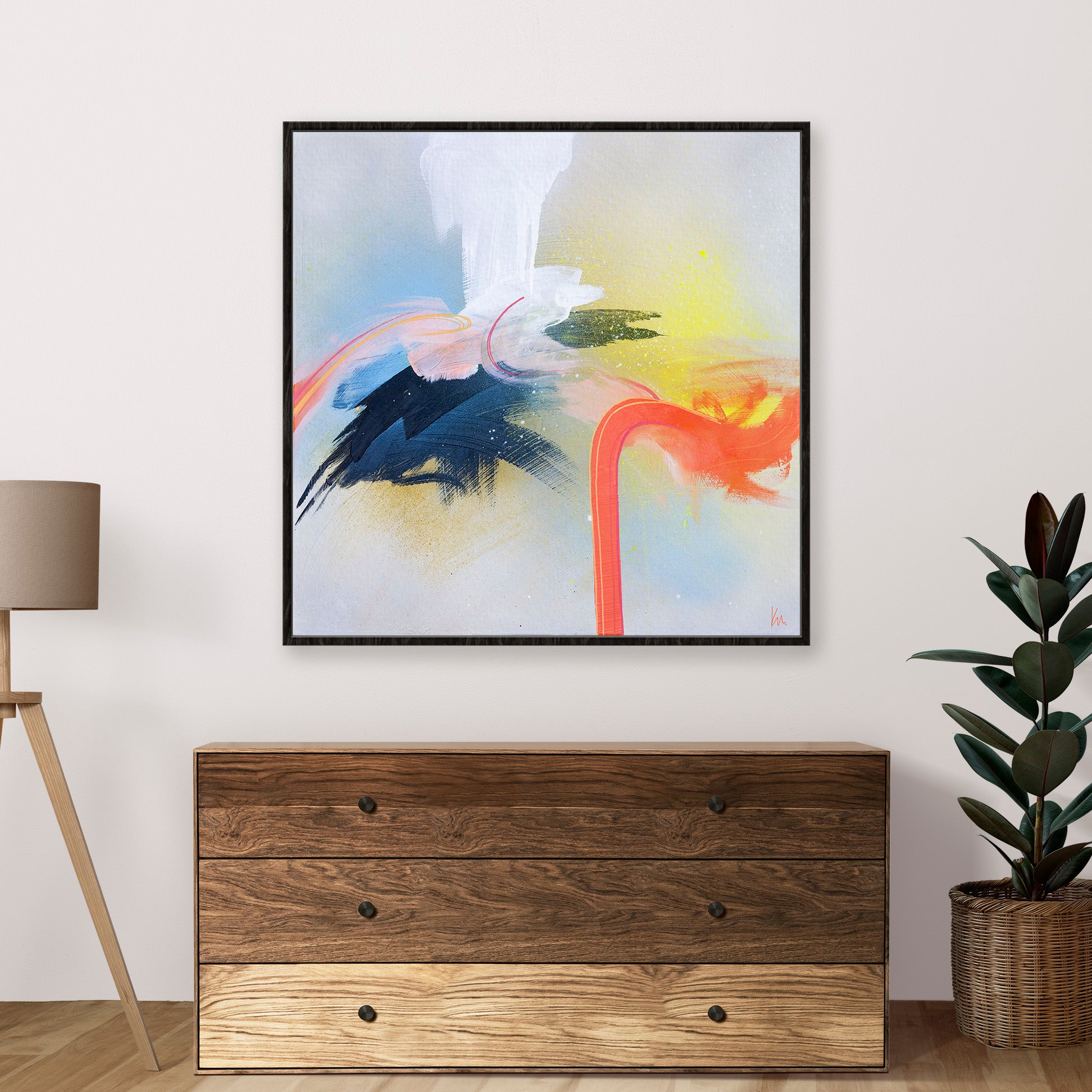 The Kate Mayer "Miami Flamingo" abstract painting, showcasing vibrant orange, blue, and white strokes, is elegantly framed and displayed above a wooden dresser beside a tall plant, crafting an inviting artistic ambiance. Let me know if you need additional product details or potential SEO keywords.