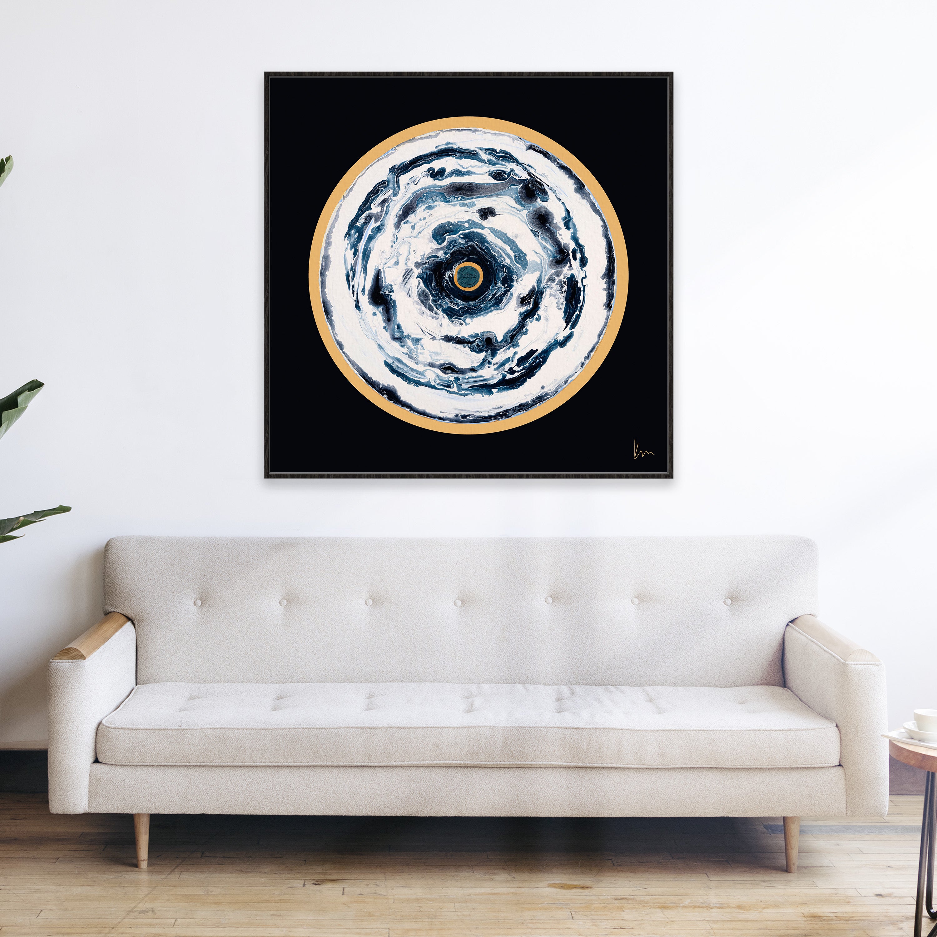 A minimalist room showcases a beige sofa beneath "Oceans Of Love," an enchanting piece by Kate Mayer that features mesmerizing swirls of blue and gold on a black background.