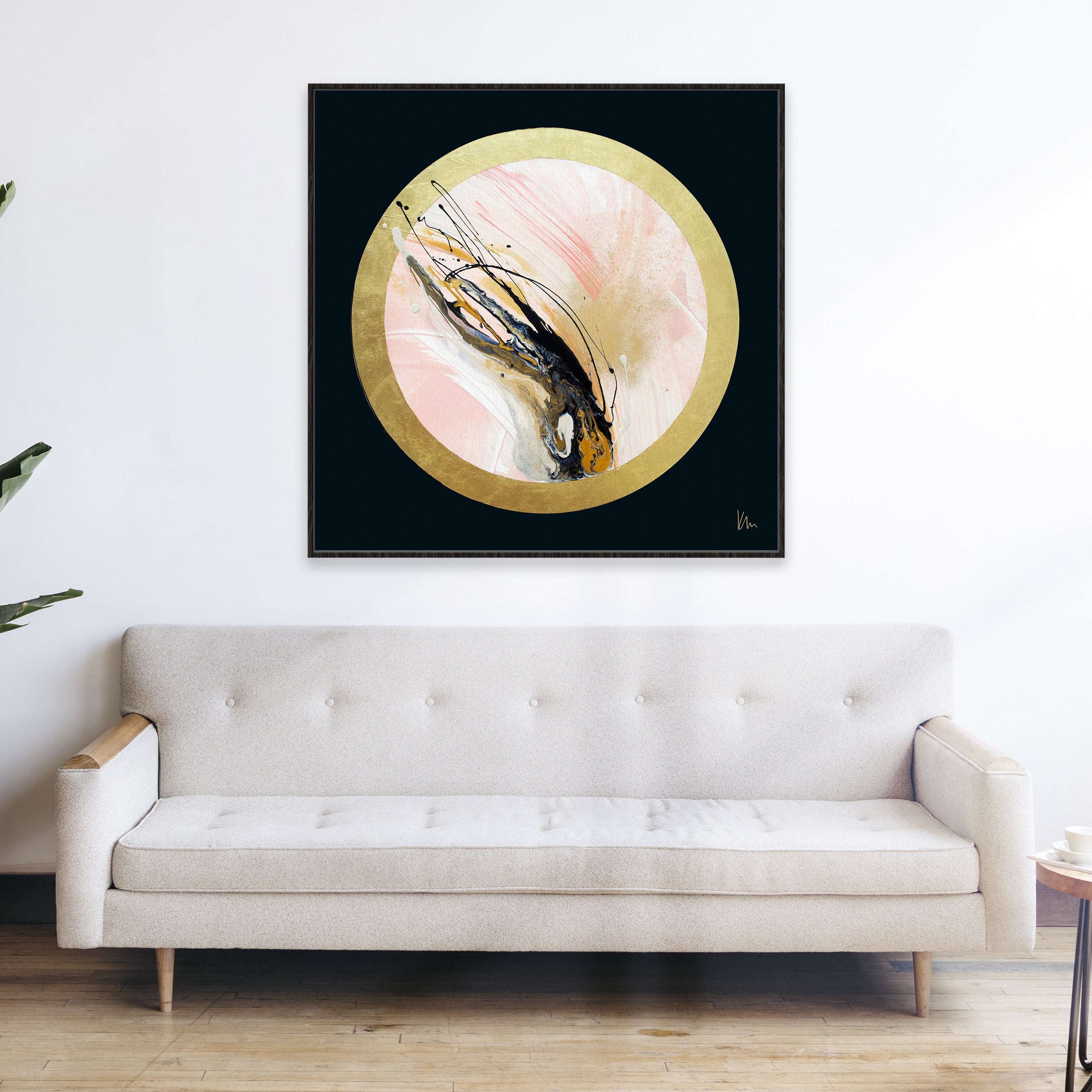 A minimalist living room with a beige sofa and the "Rise Up" artwork by Kate Mayer, featuring gold, black, and pink tones on the wall above it, creates an elegant atmosphere.