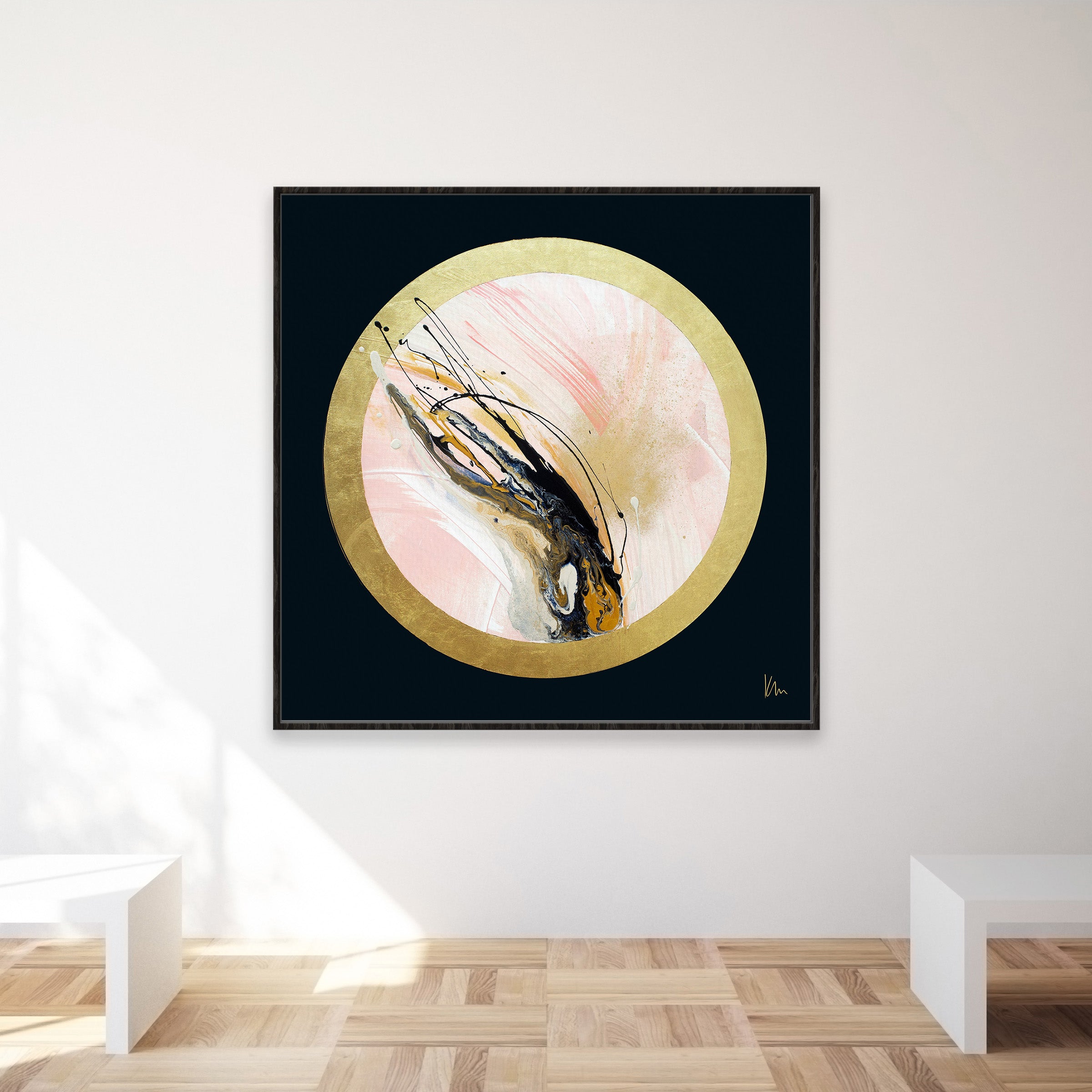 Rise Up," an abstract painting by Kate Mayer, features gold, black, and soft pinks encased in a circular frame. Centered on a white wall in a minimalist room, this artwork exudes subtle elegance and modern chic.