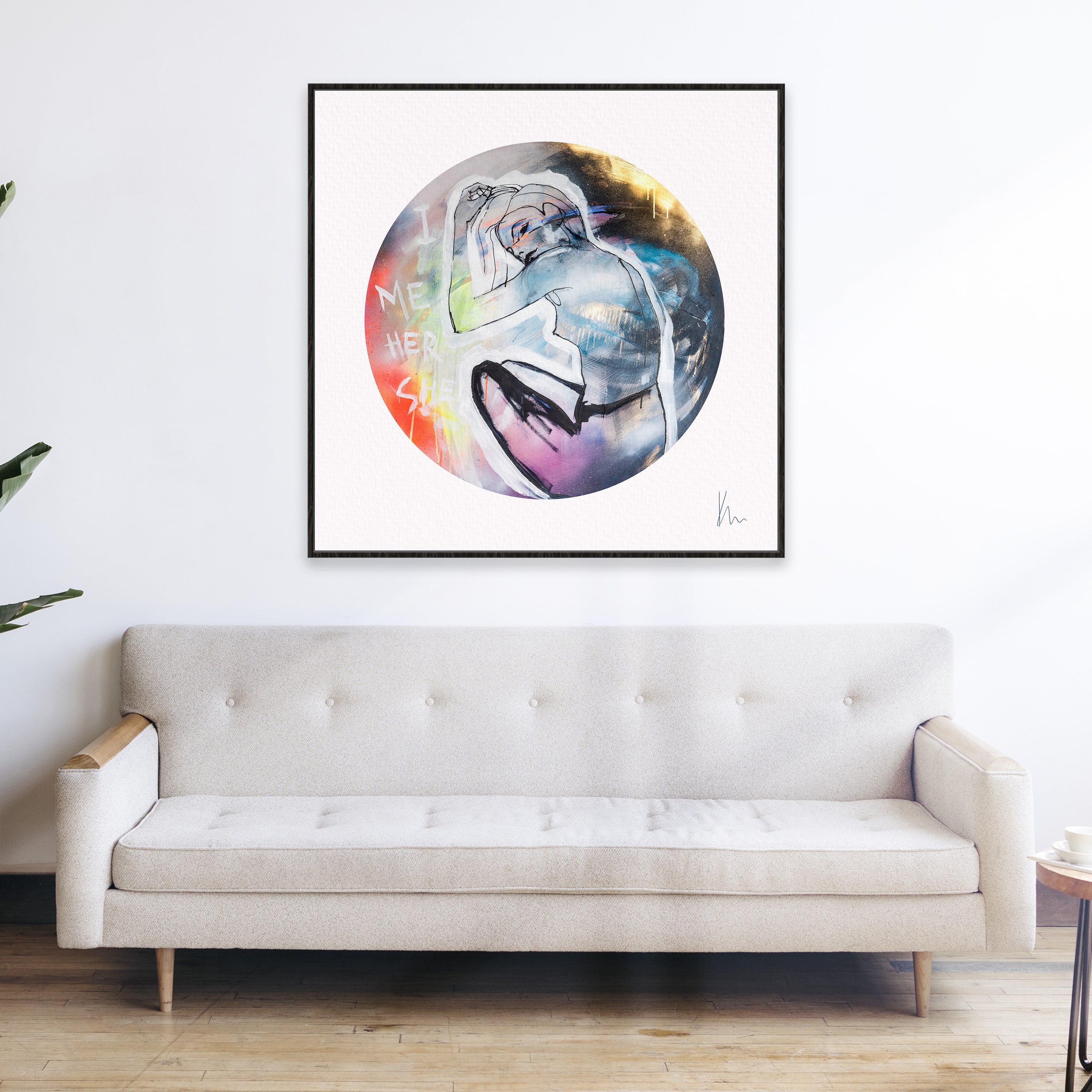 A colorful abstract painting titled "She" by Kate Mayer is elegantly displayed on a white wall above a beige sofa with wooden elements, creating a captivating scene.