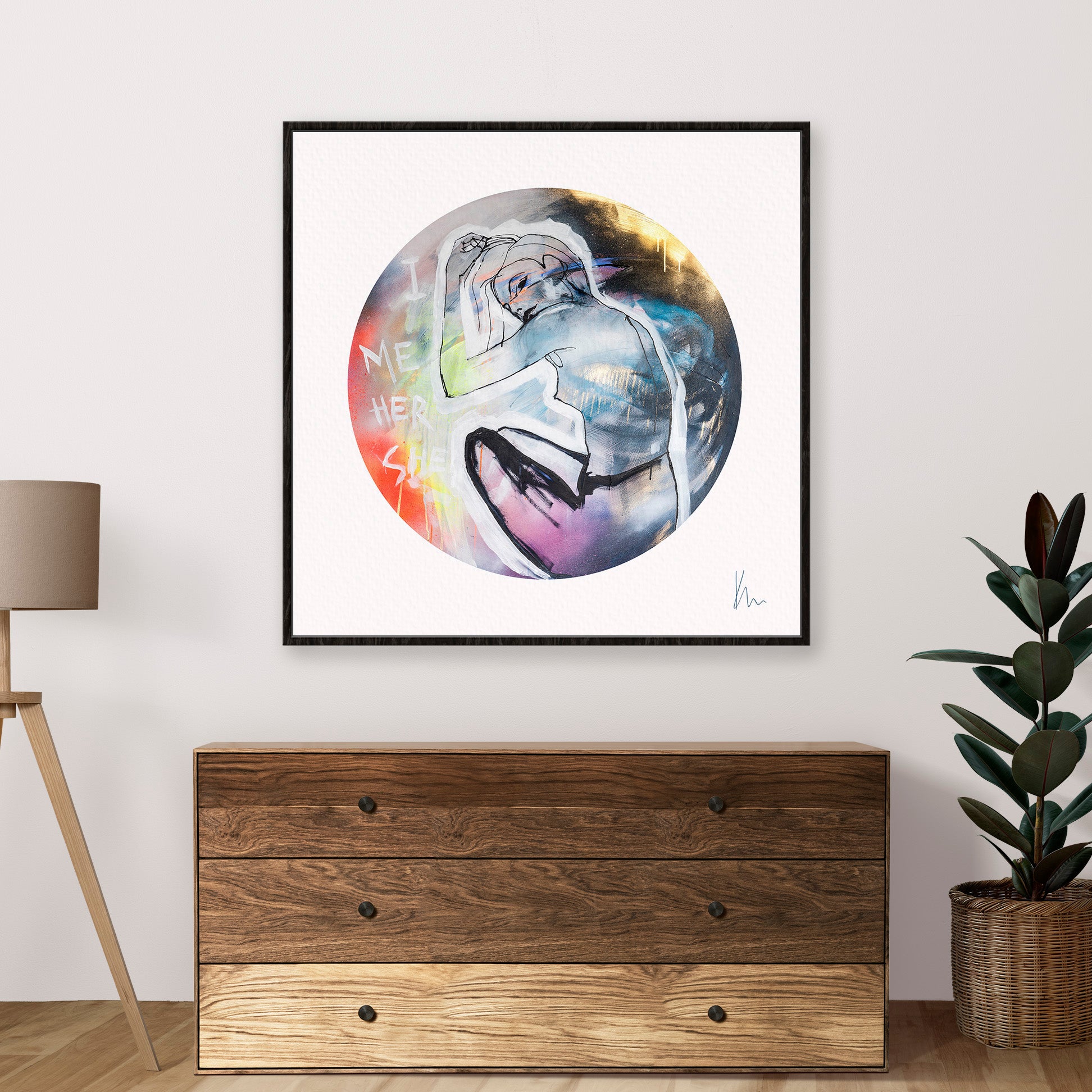 A framed abstract artwork titled "She" by Kate Mayer, featuring a figure in a circle, is hung above a wooden dresser; beside it, a lamp and potted plant complete the arrangement.