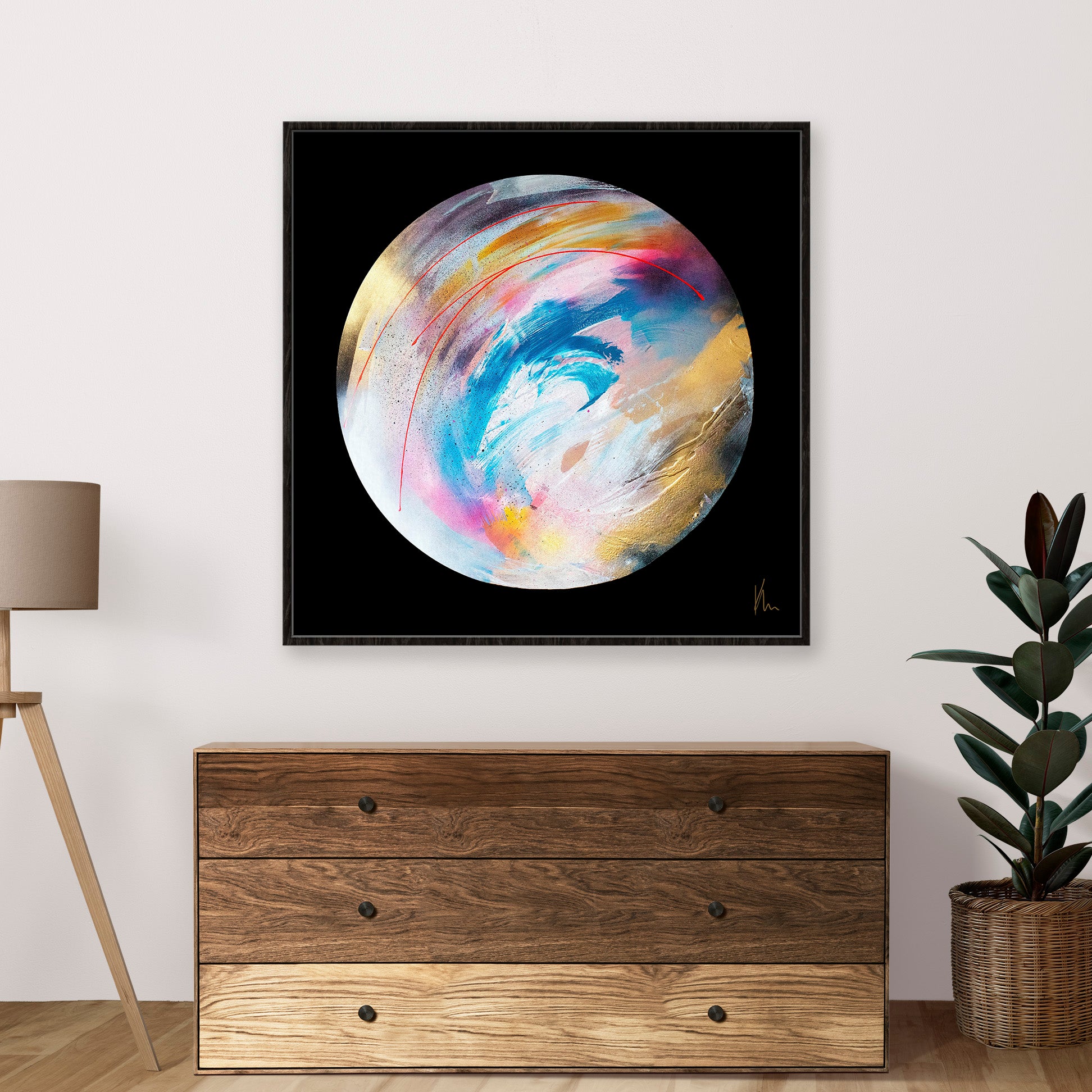 The "Speak Your Truth" abstract circular painting by Kate Mayer, with its colorful swirls, brightens the white wall above a wooden dresser. A plant and lamp sit on either side, adding balance to this vibrant display.